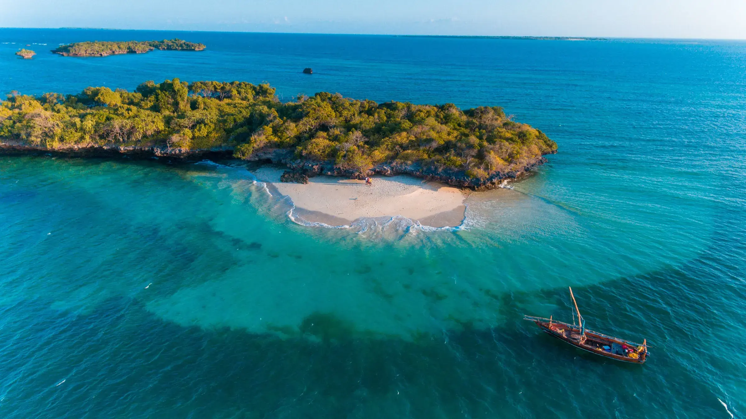 A dhow crosses the clear shallows off Zanzibar, an islet set in turquoise.
