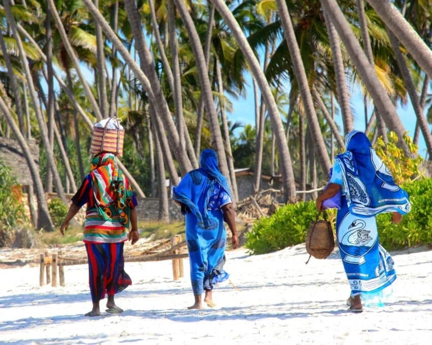 Three women in bright wraps walking on a palm lined beach
