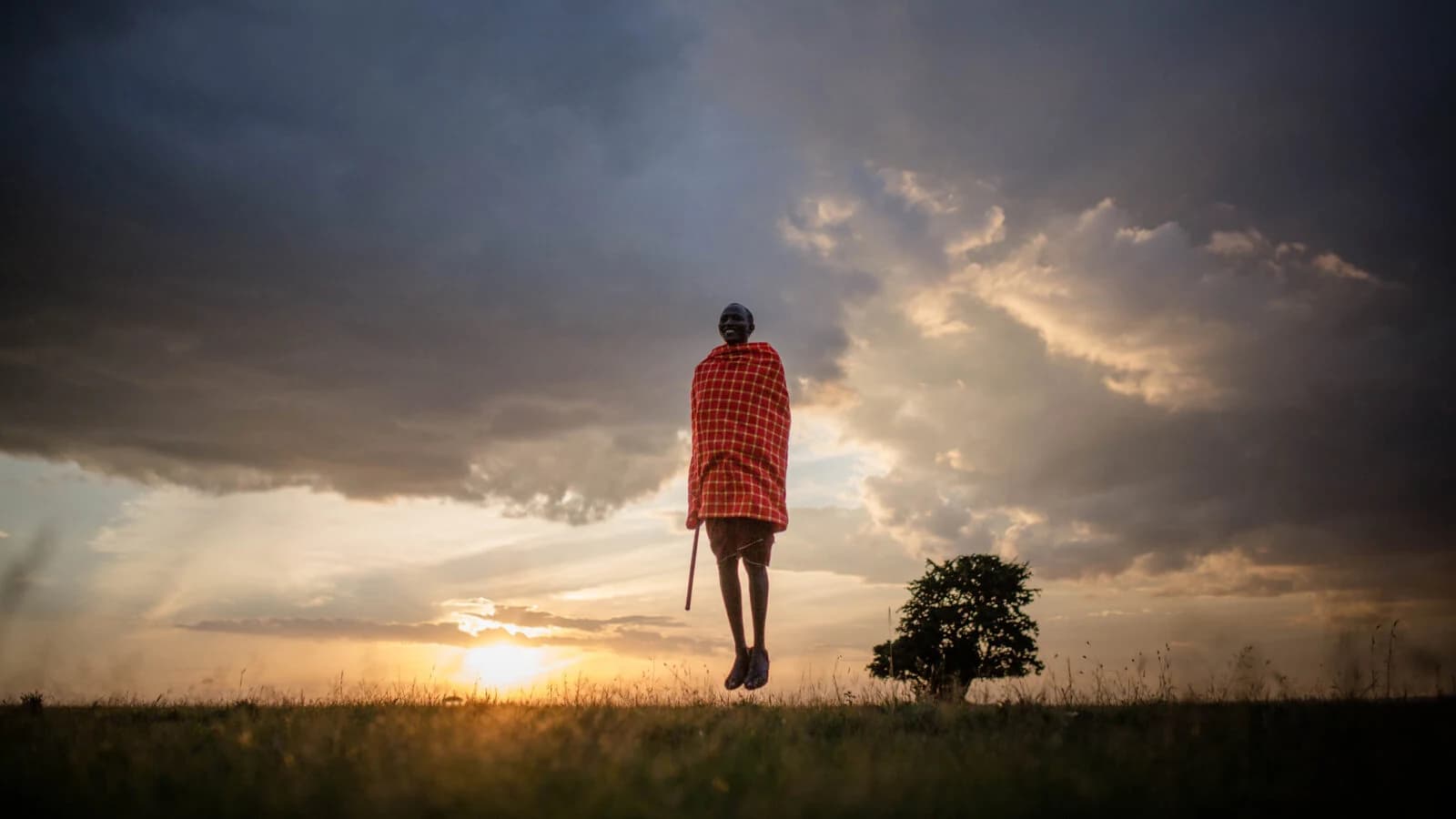 Maasai figure mid leap in silhouette against sunset storm clouds