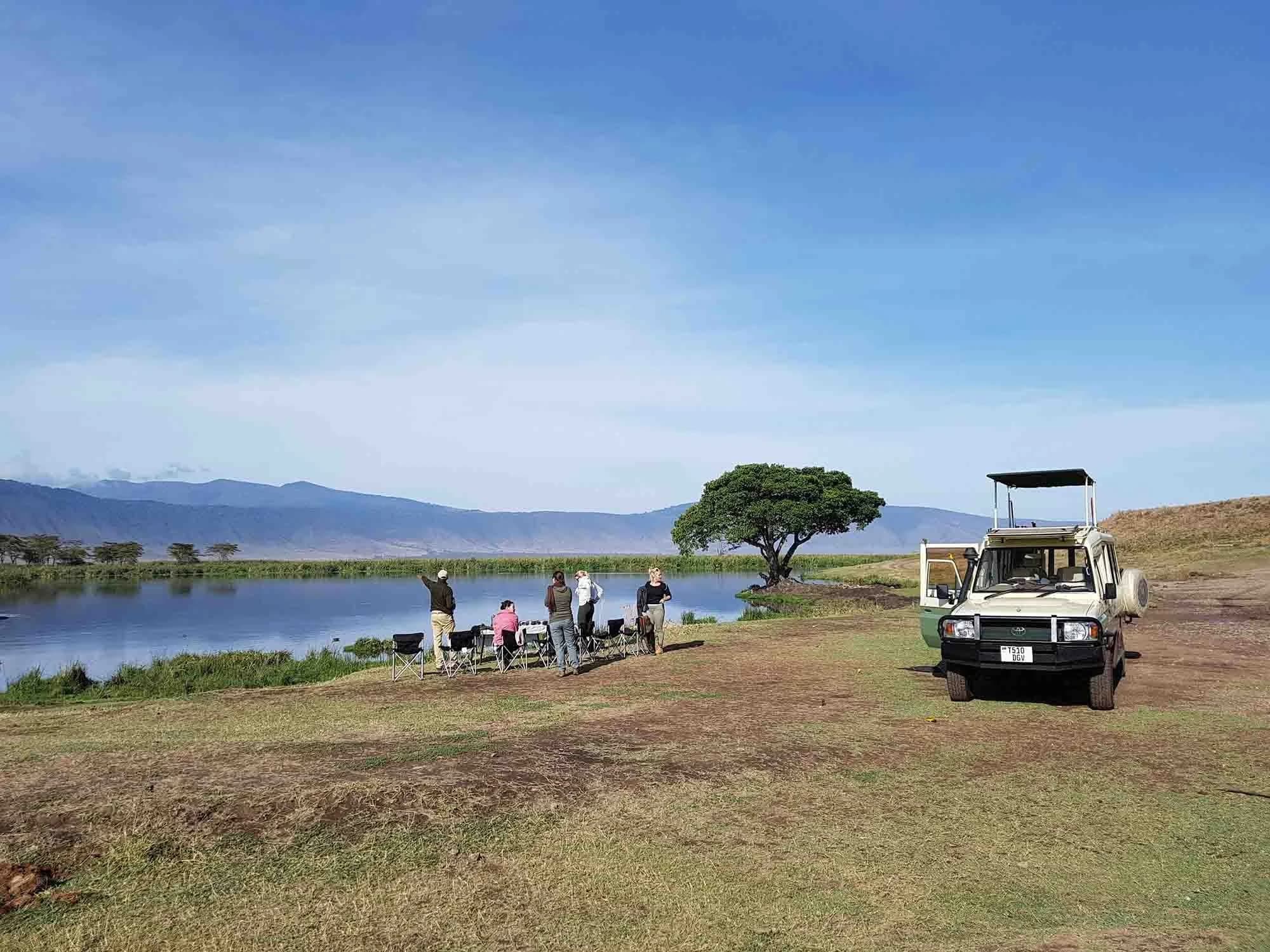 Safari vehicle and guests by a lake with crater rim beyond