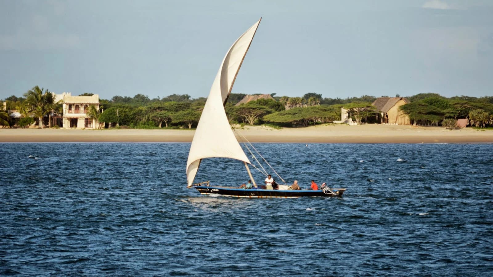Dhow with white lateen sail crossing blue channel
