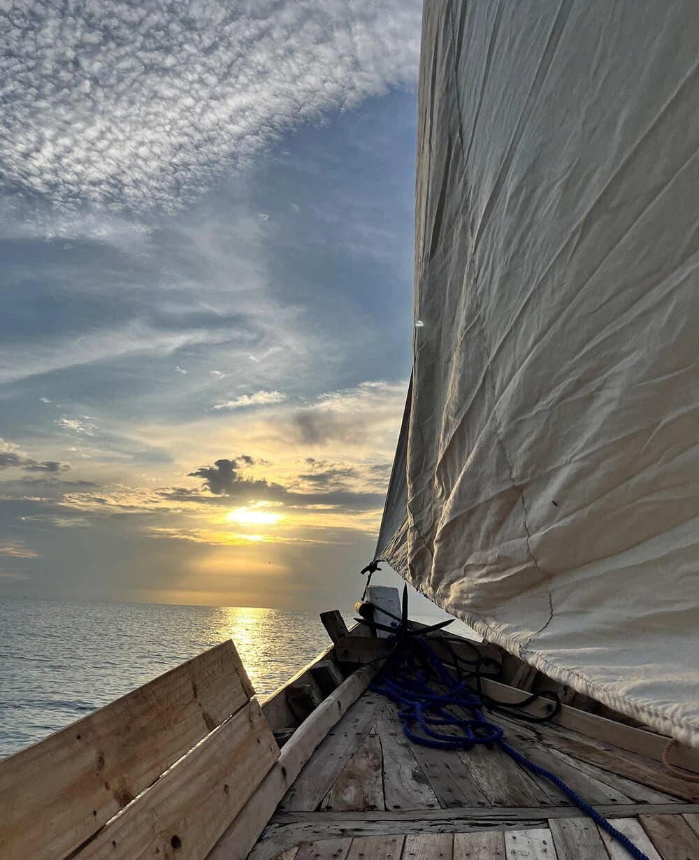 View from a dhow deck: billowing sail, sunset sky and sea