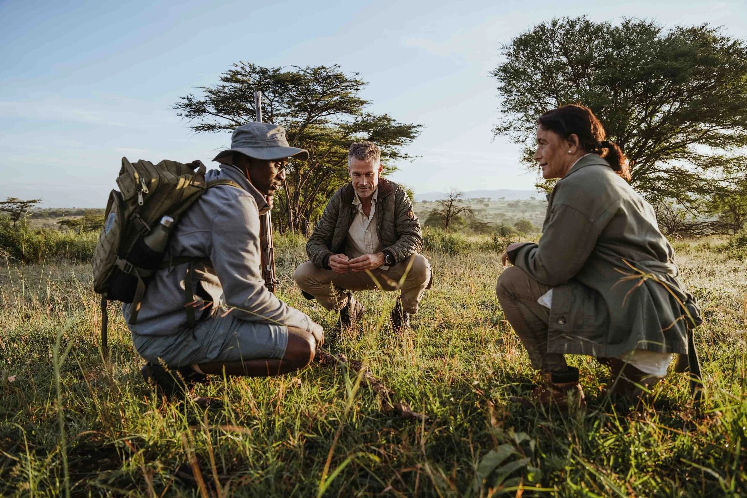 Guide and two guests crouching in grass on a walking safari