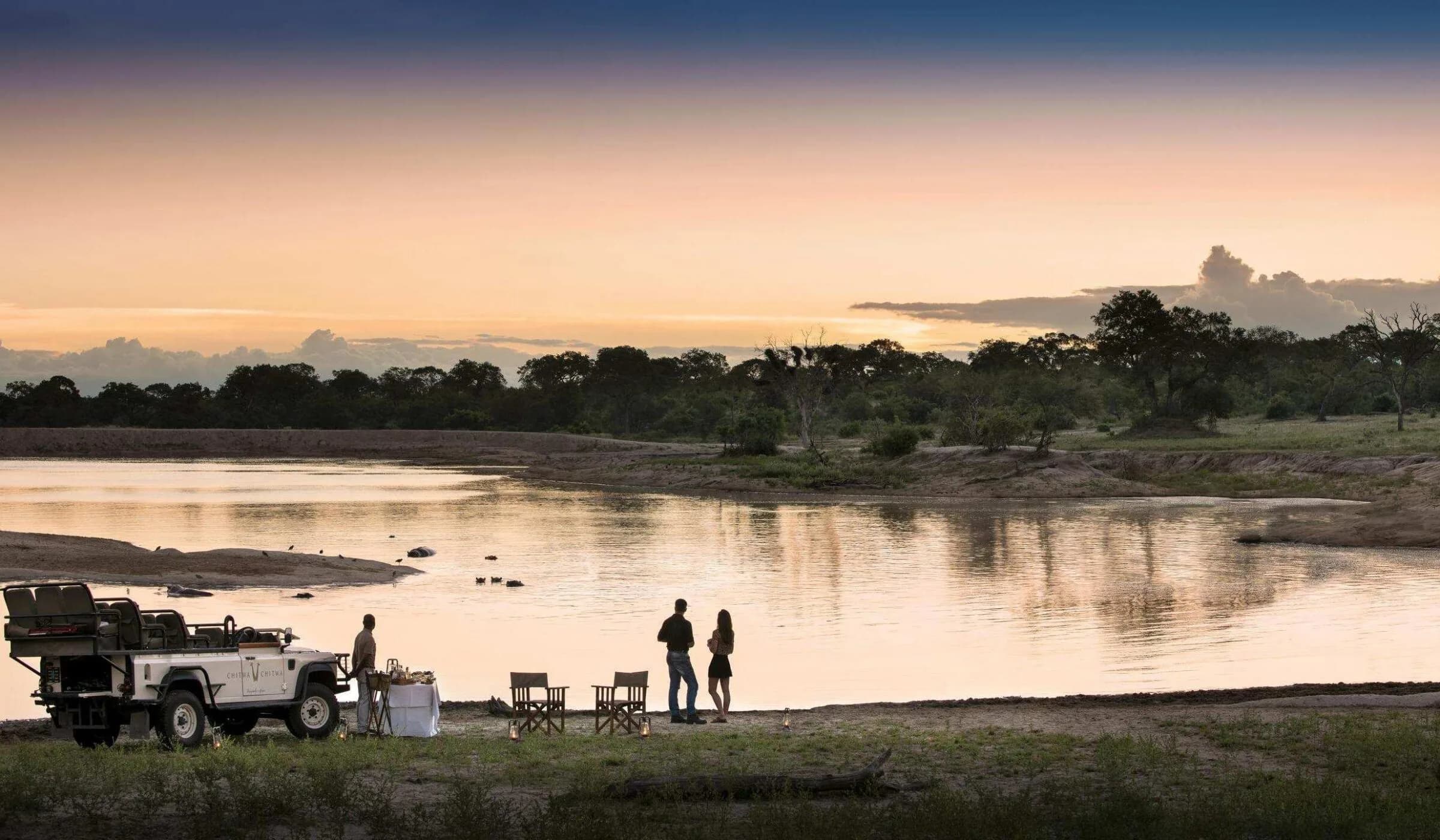 Temporary image: a couple beside a river at sunset next to a safari vehicle