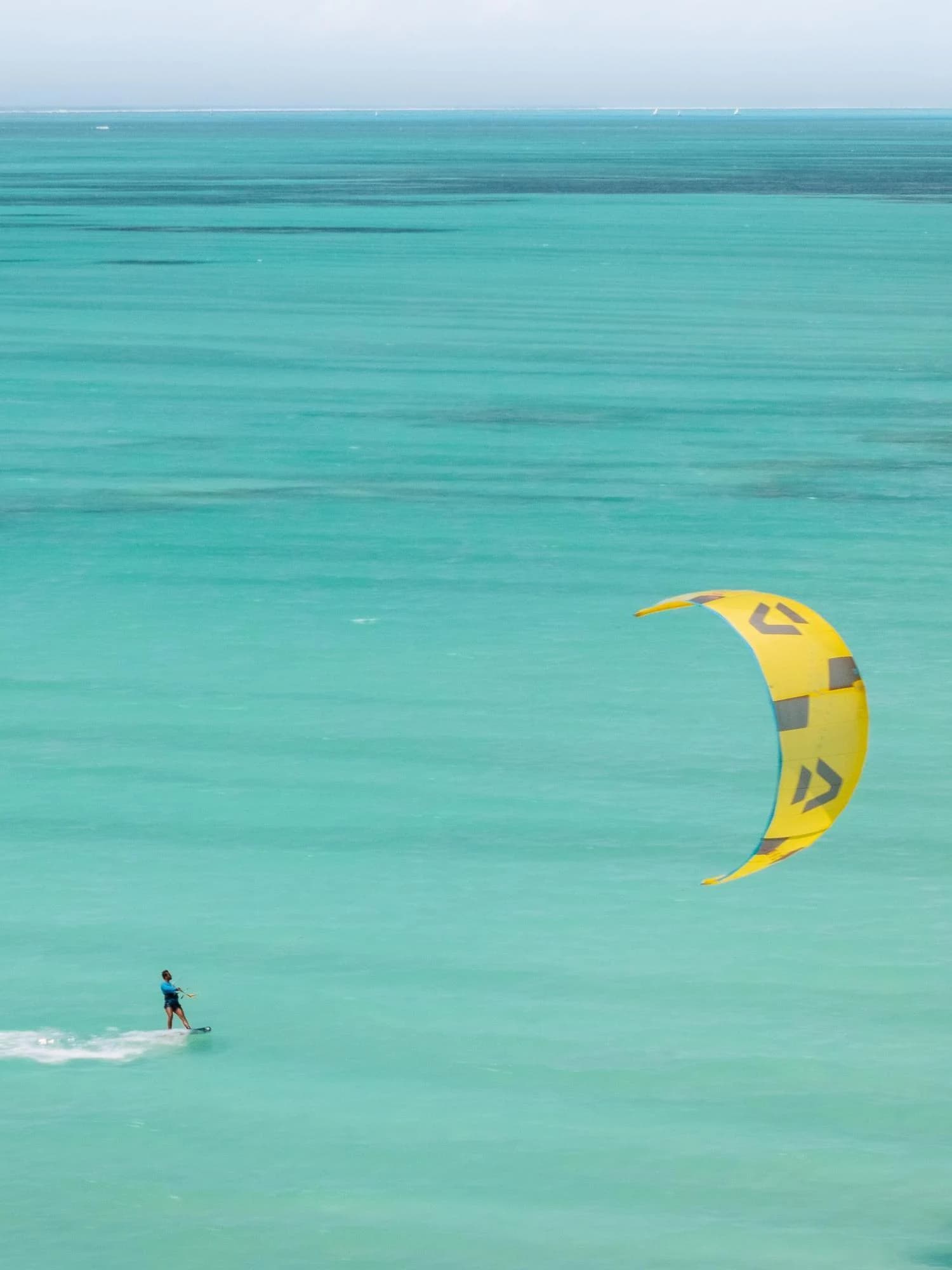 Aerial of a kitesurfer with yellow kite over turquoise water
