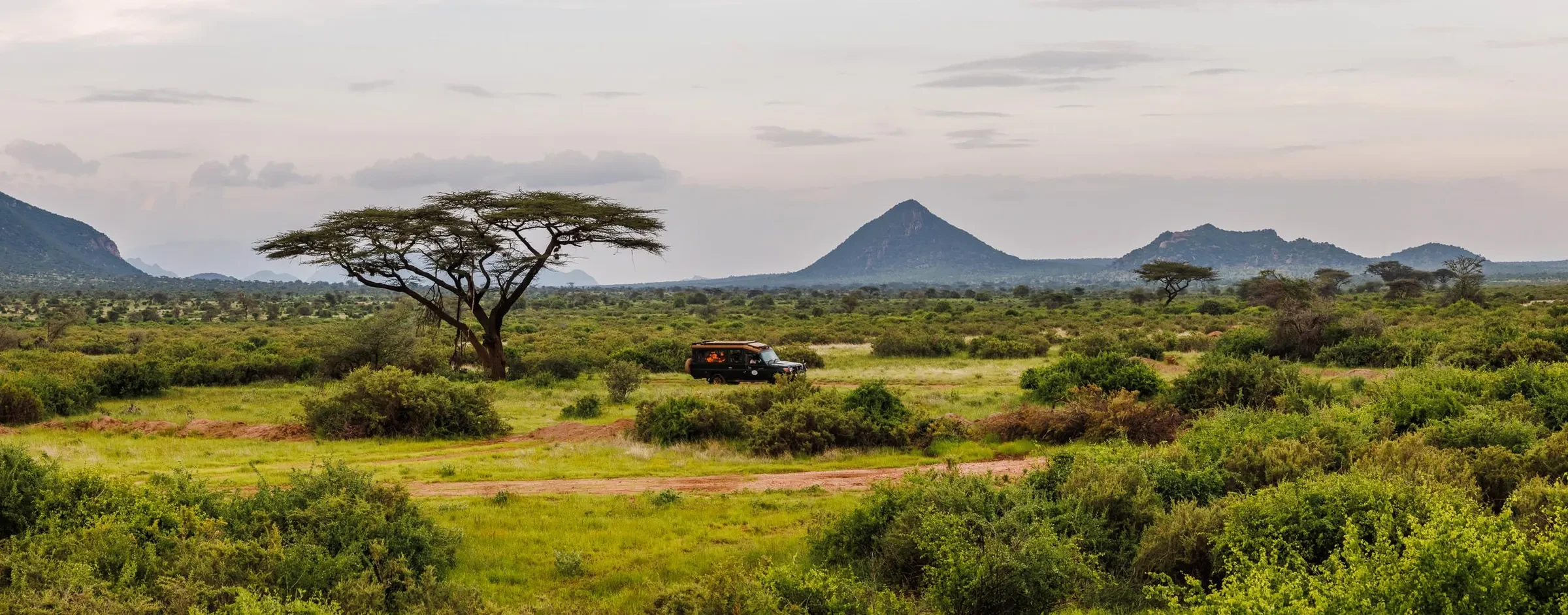 The Samburu bush runs green toward the old volcanic hills, a vehicle small on the plain.