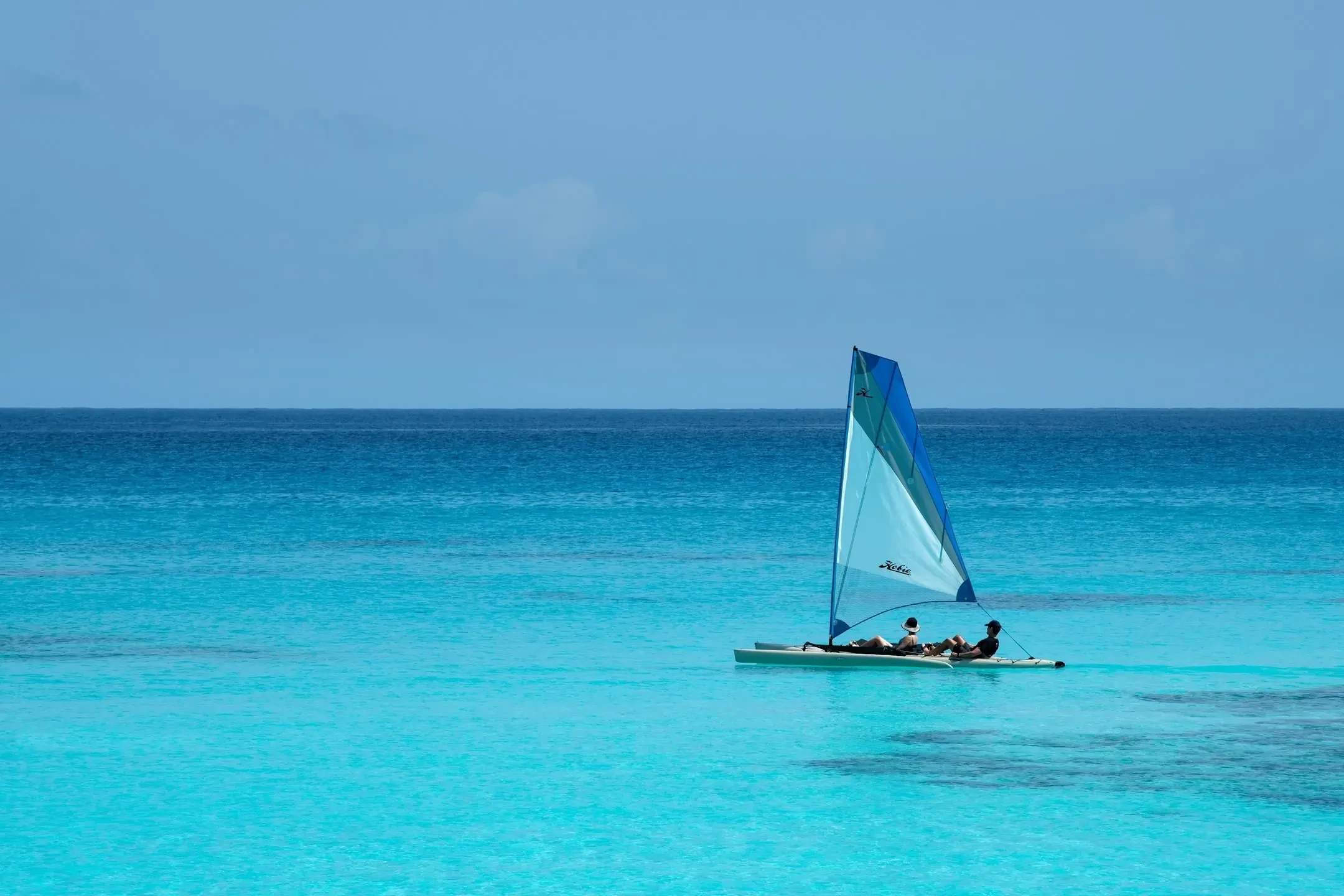 A catamaran crosses the turquoise off Mnemba, the island low beyond.