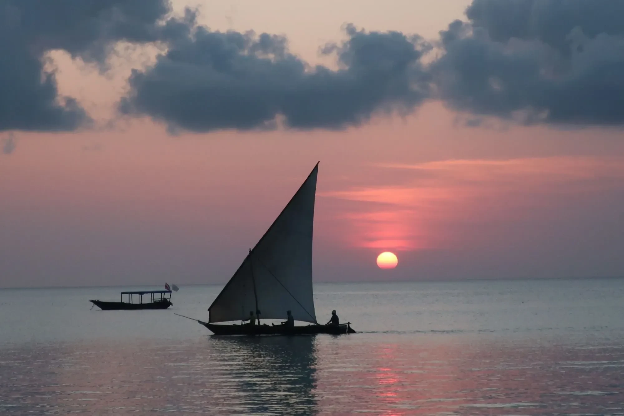 A dhow crosses the still water under a burning sky, the sun going down over the Indian Ocean.