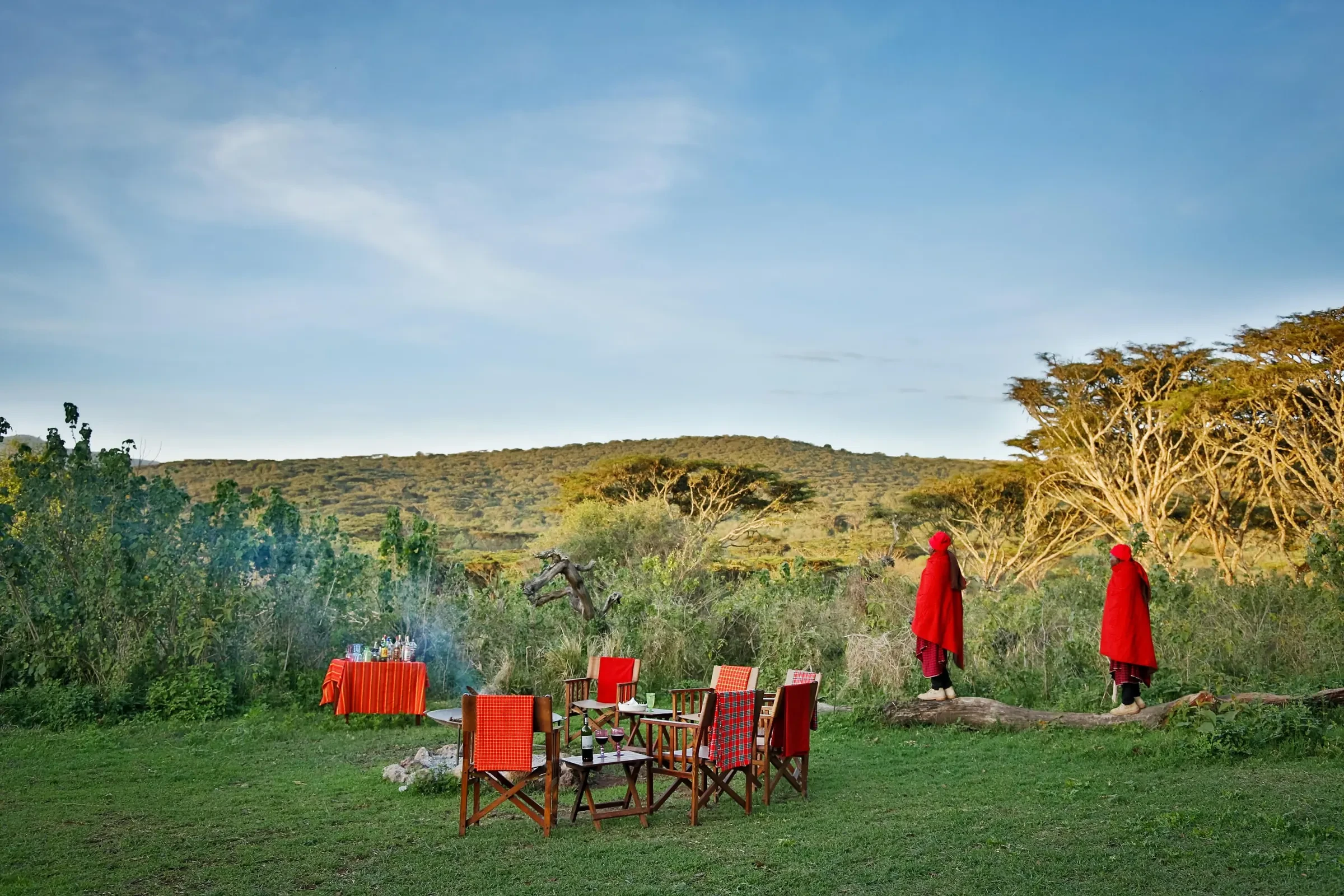 Two figures stand in the last light as camp is set for sundowners, the acacia backlit gold.