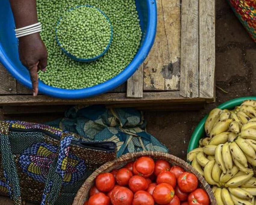 Top down view of market vendor's hand by bowls of peas, tomatoes, bananas