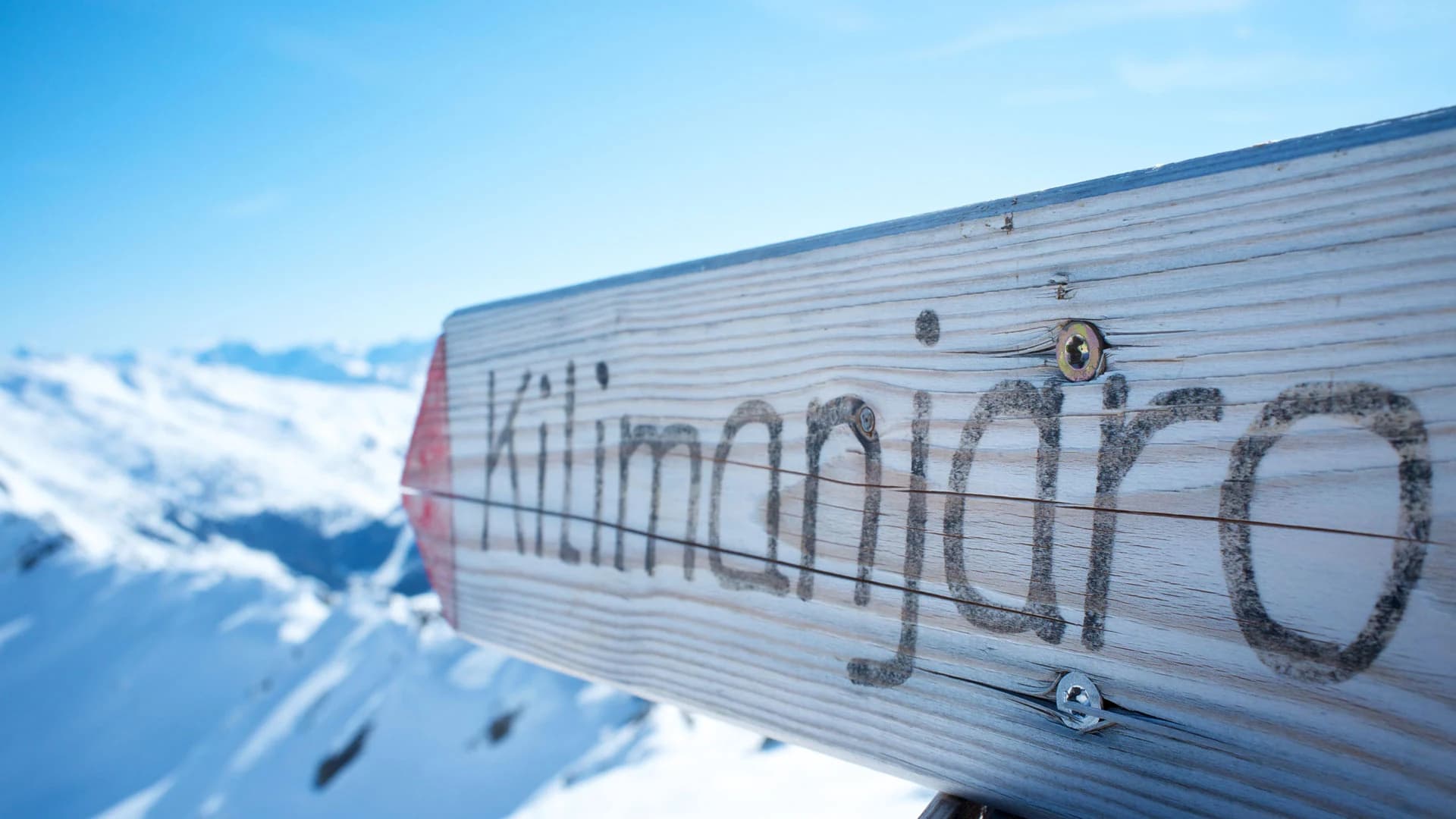 Wooden Kilimanjaro signpost over snow with blue sky