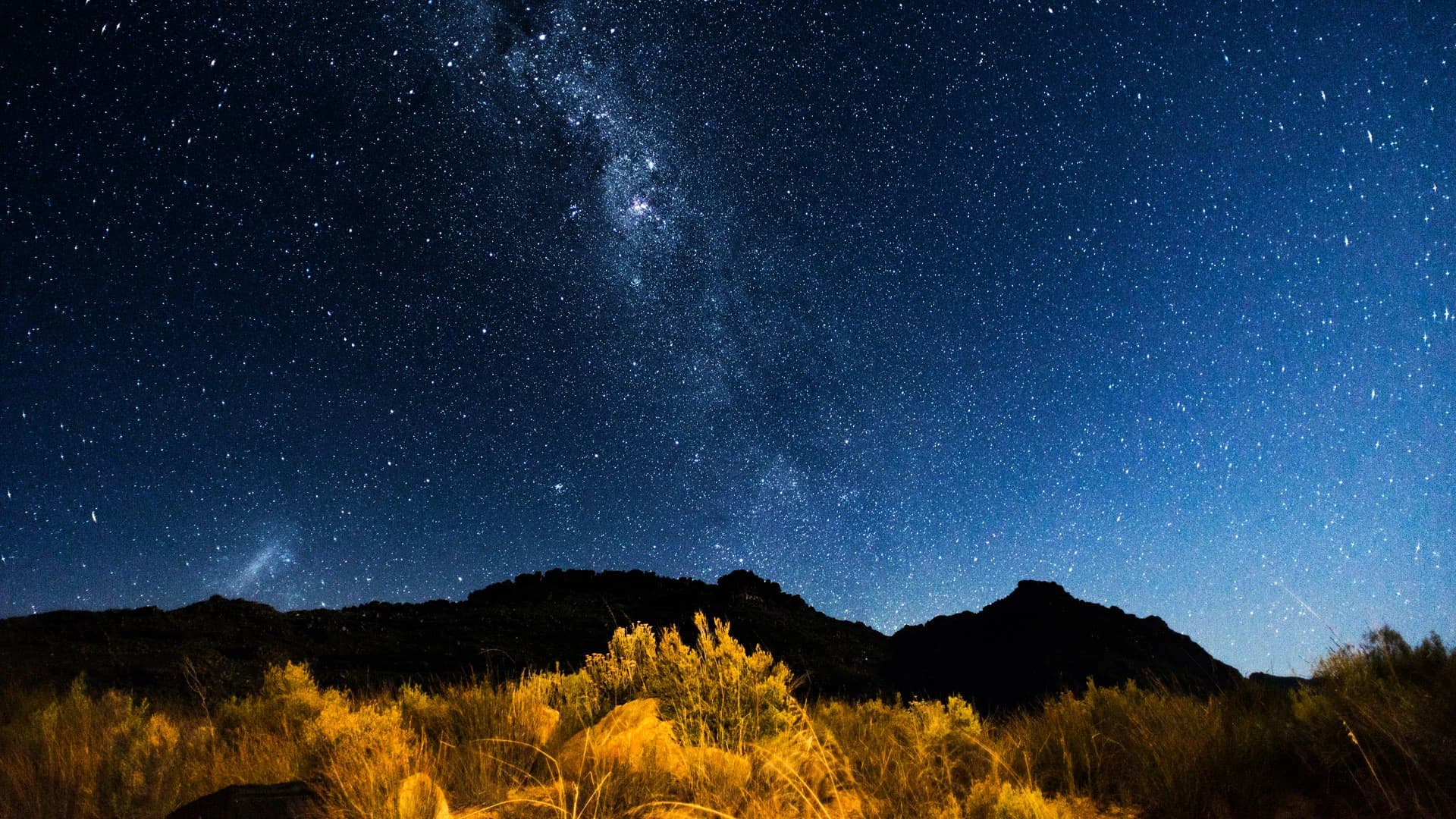 Milky Way over dark hills with a glowing bush foreground