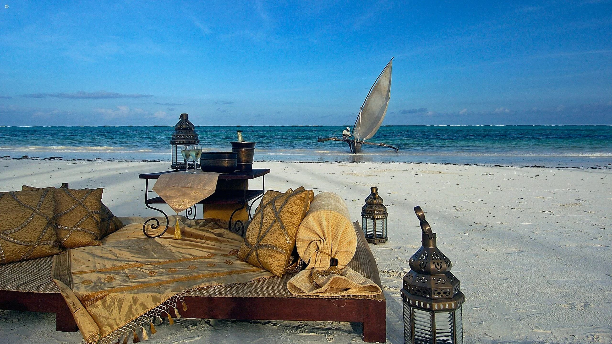 Beach daybed with cushions and lanterns, dhow sailing behind