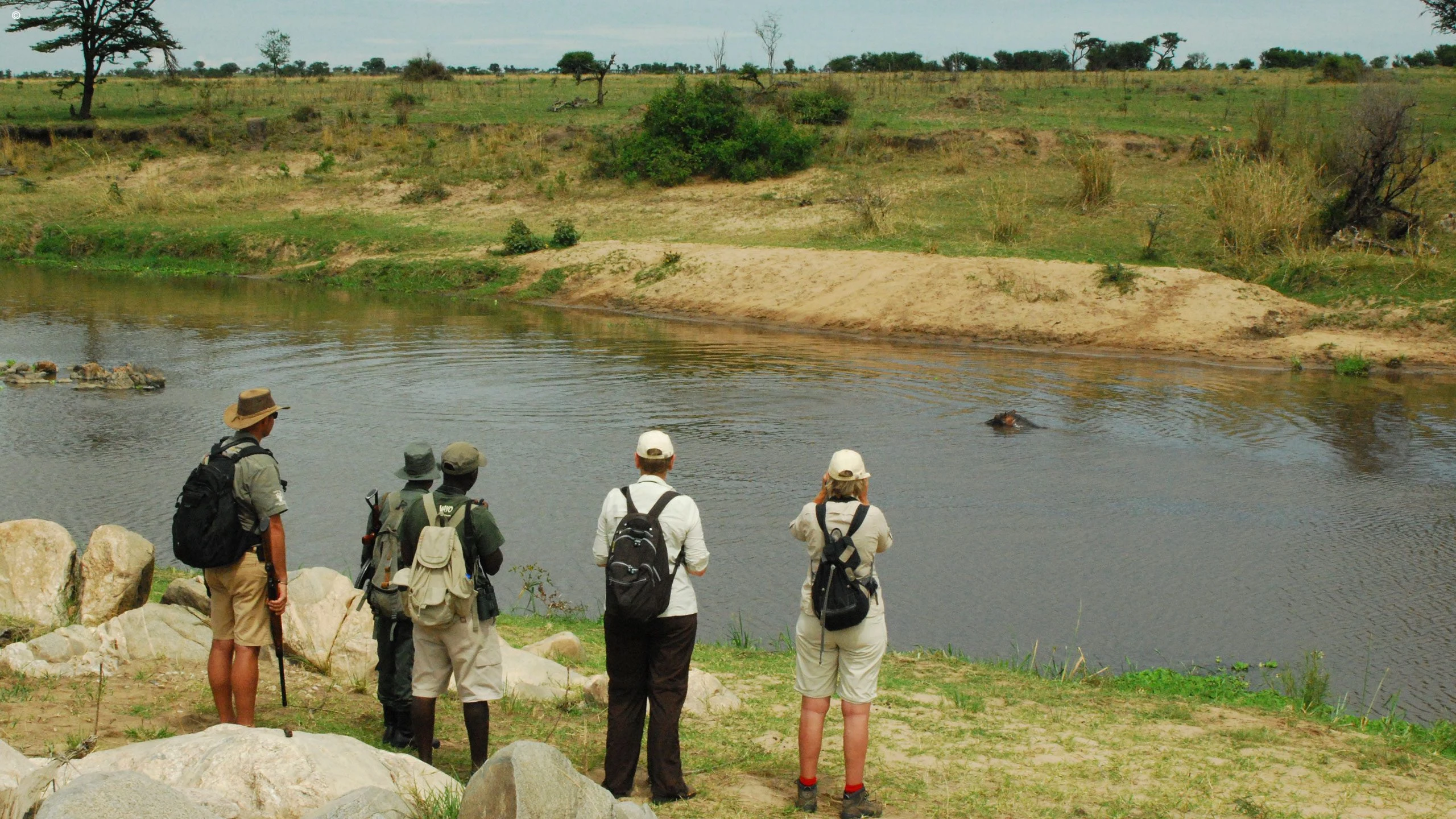 Walking group with guides beside a river in the Serengeti