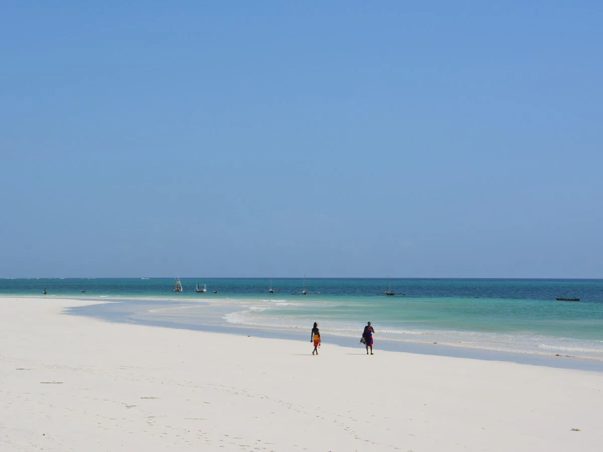 Two people walking along a wide white beach beside turquoise water