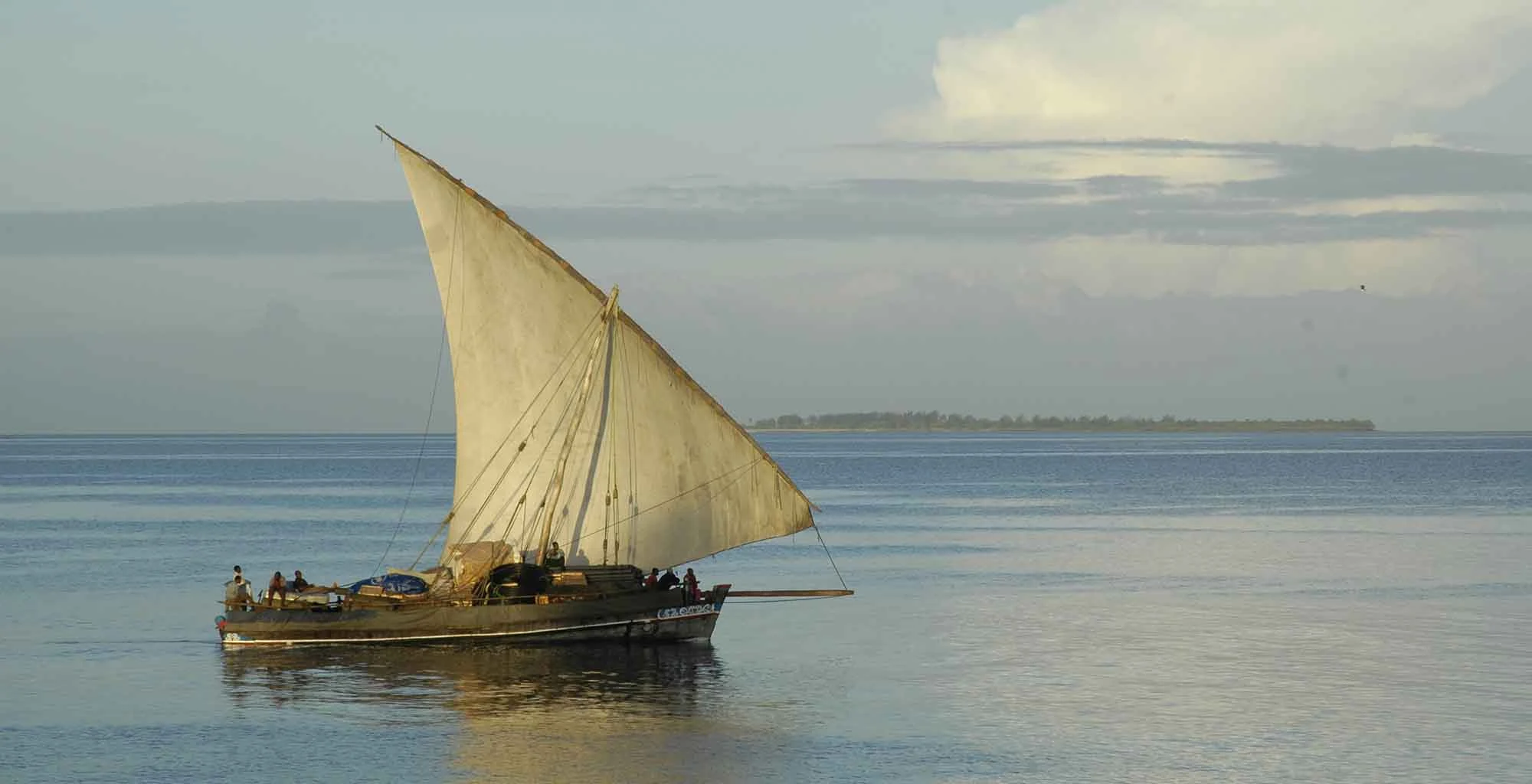 A traditional dhow with a cream sail gliding over calm water