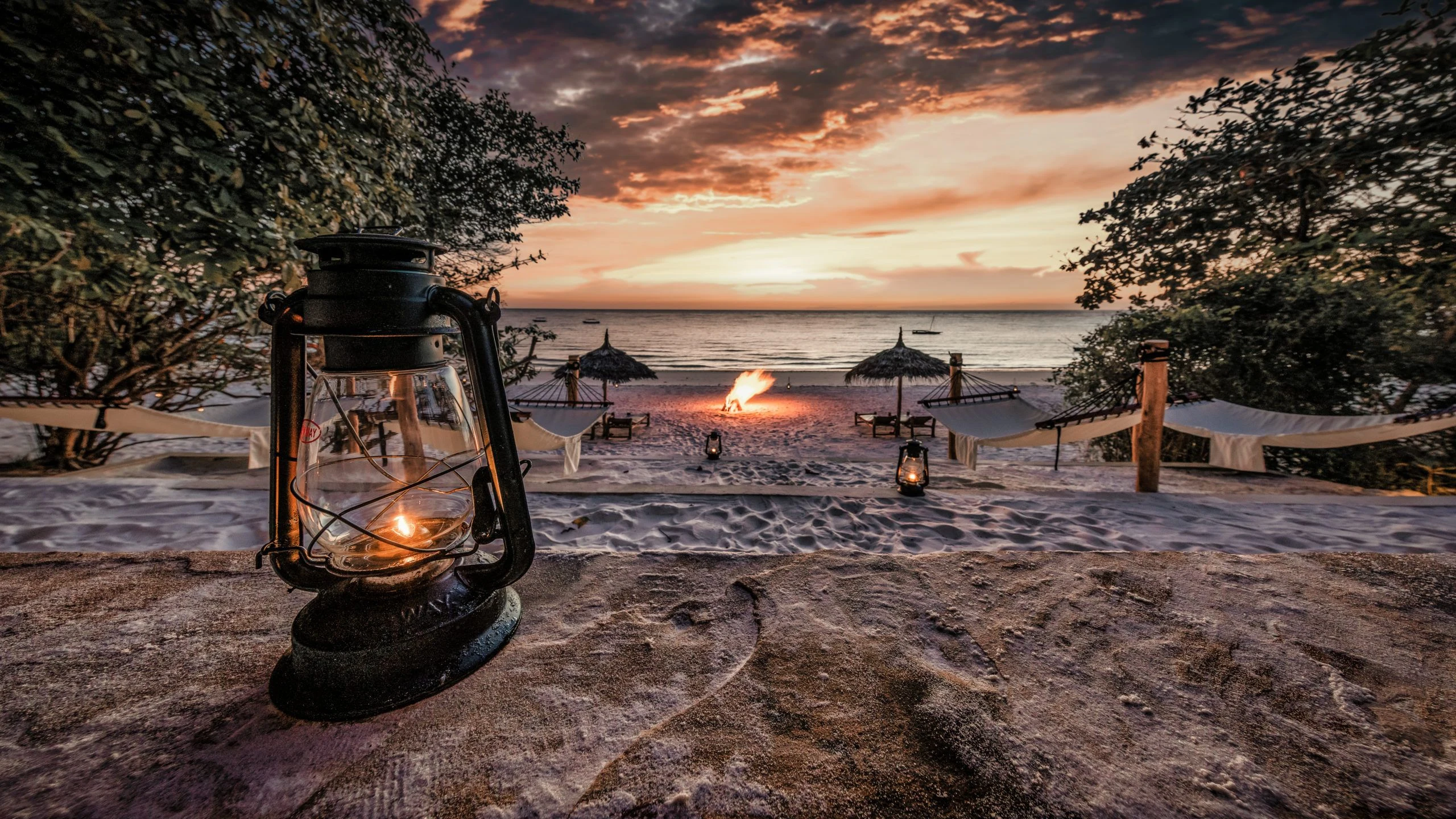Lantern and beach seating above a sandy shore at sunset
