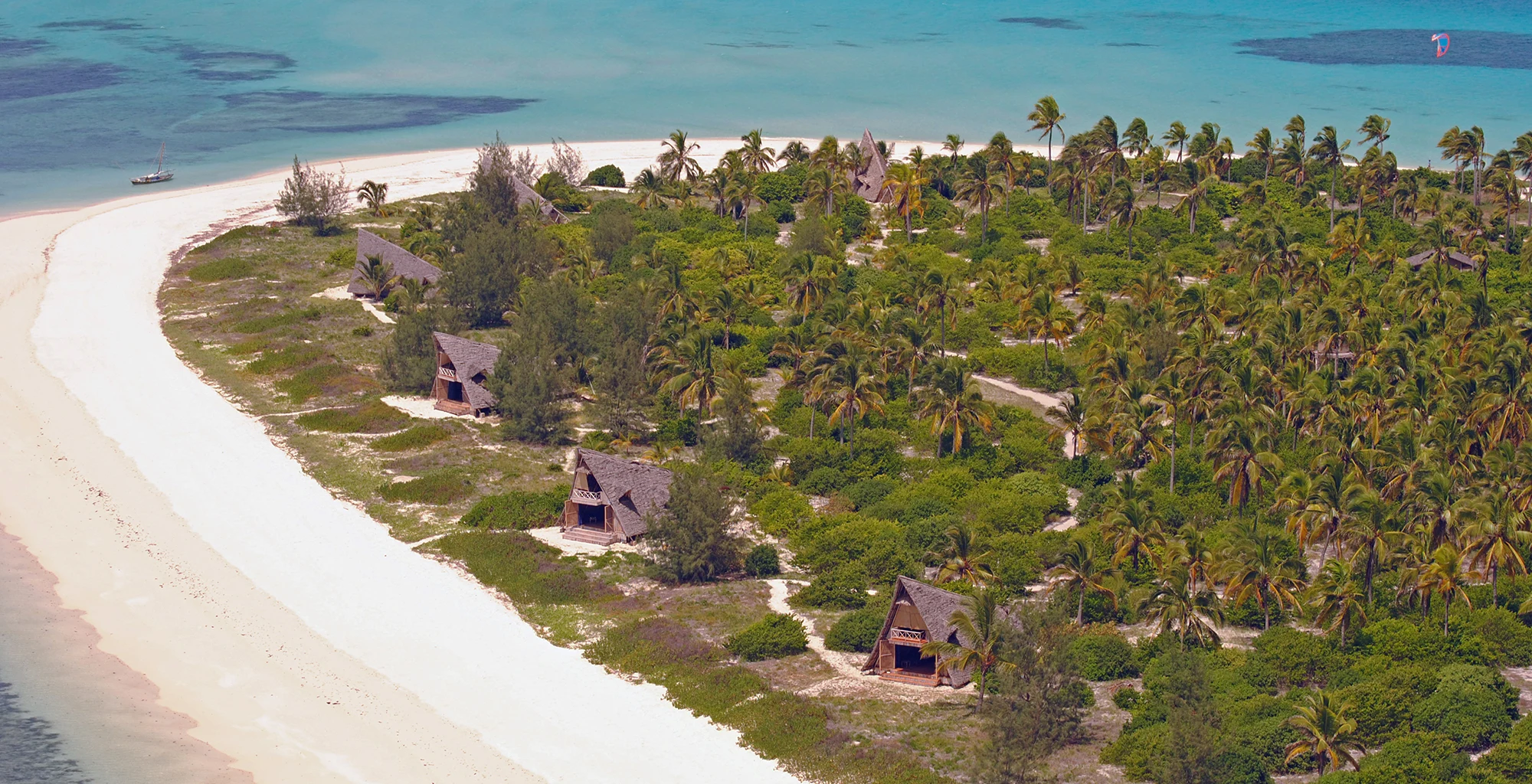 A long white beach and palm grove beside turquoise water, seen from the air