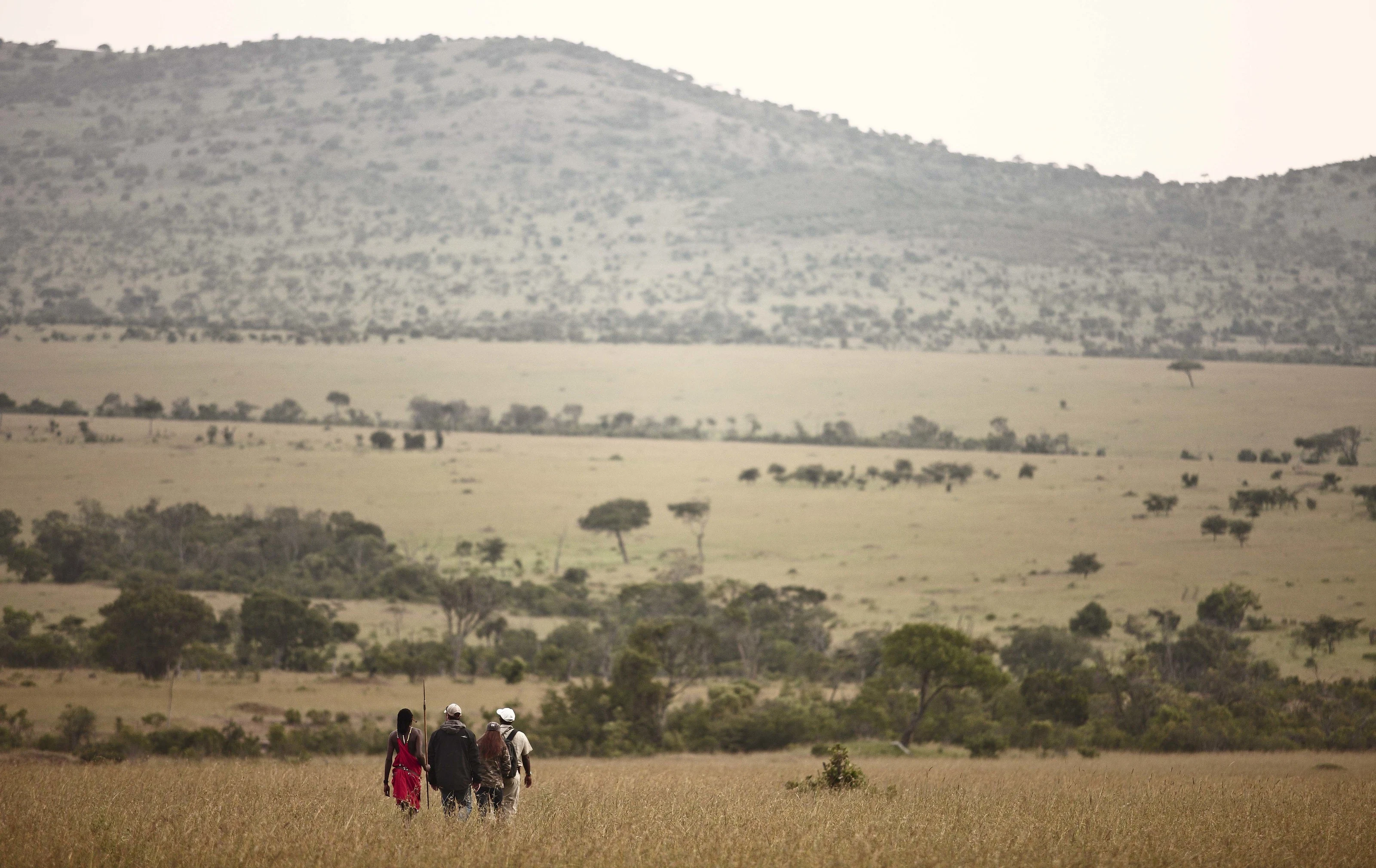 Three walkers crossing open grassland below hills in Loliondo
