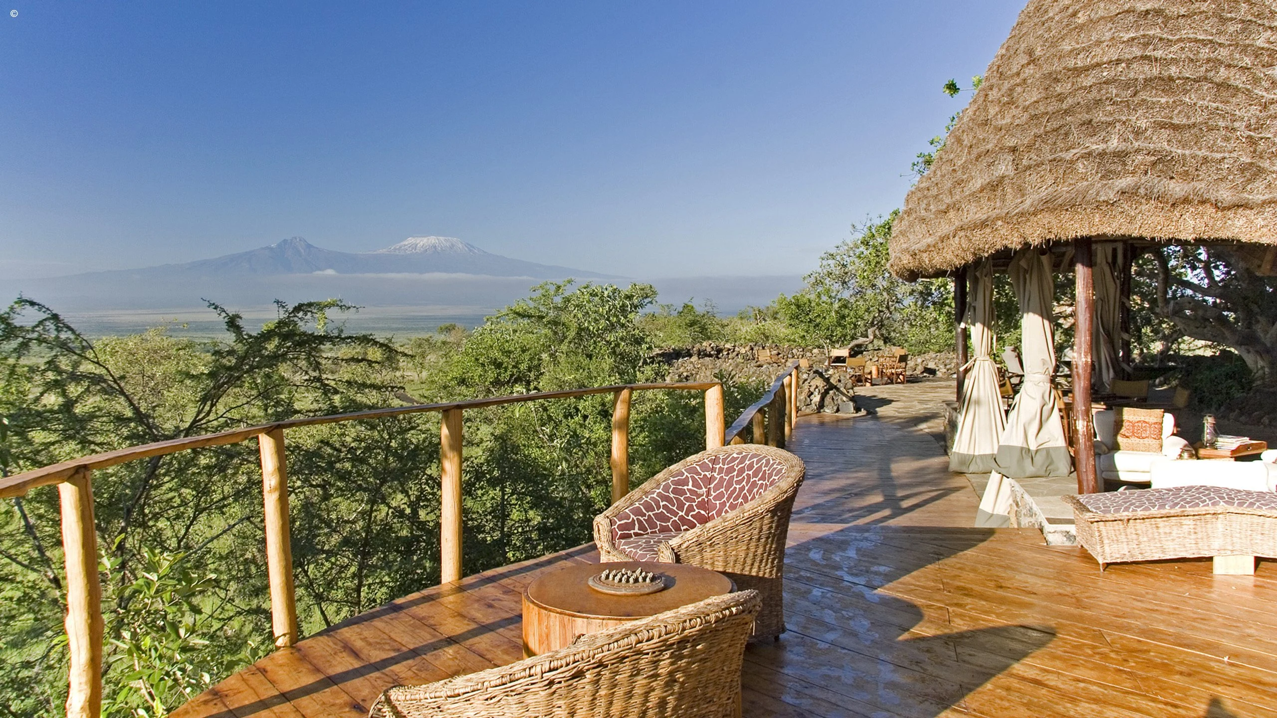 Thatched lodge deck with chairs and a view toward Kilimanjaro at Campi ya Kanzi