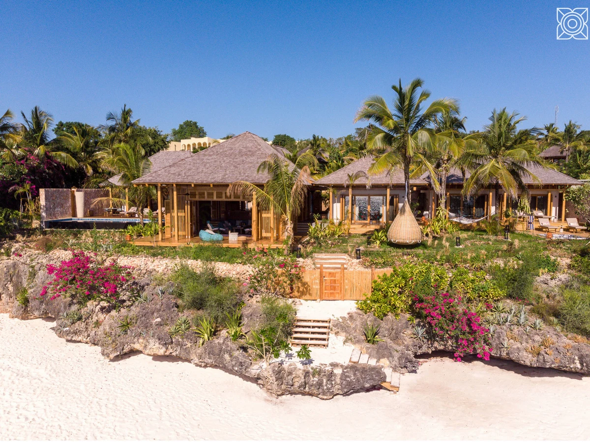 Thatched cliff top villas above a white beach in bougainvillea