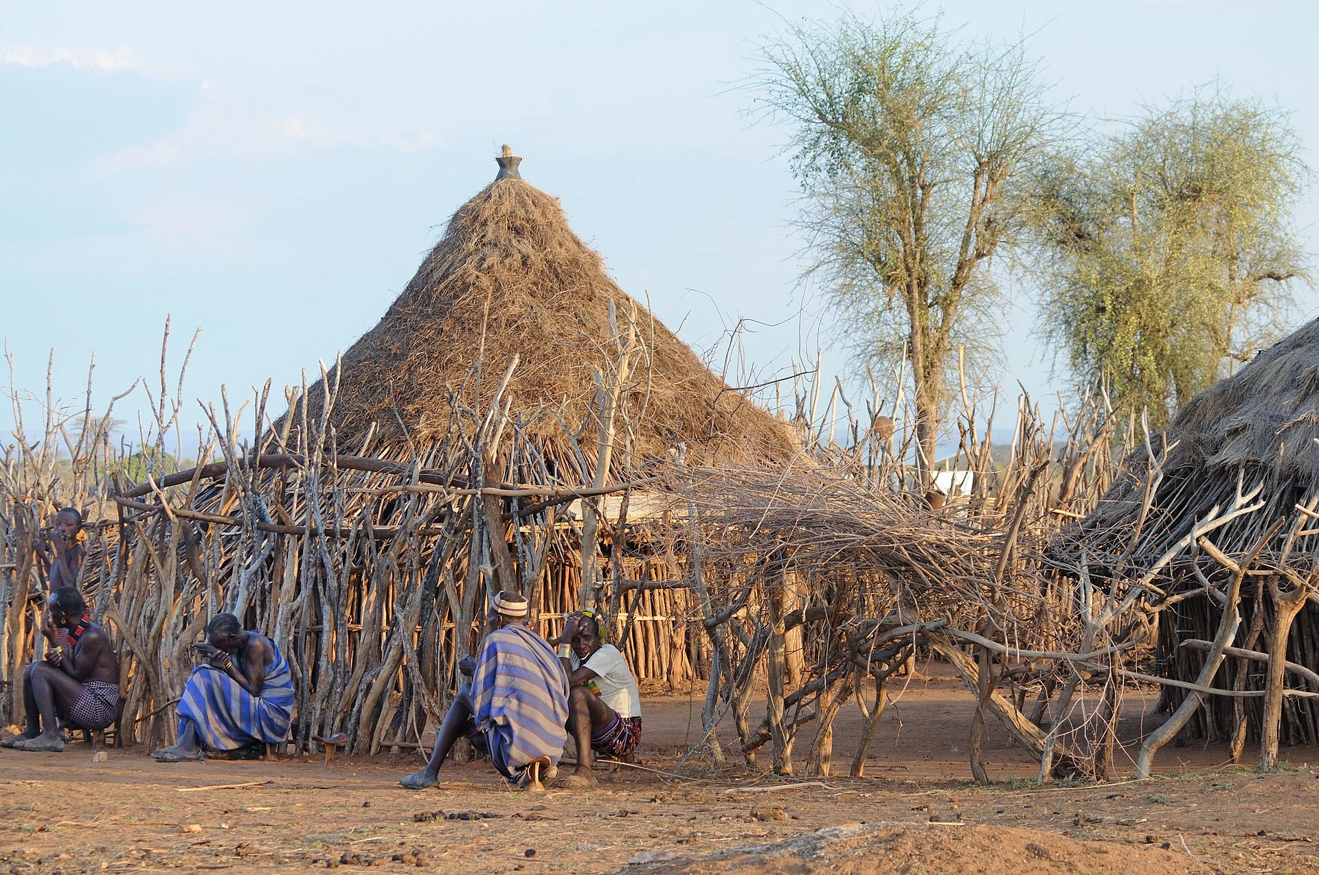 Hamar men sit beside traditional thatched huts in their village.