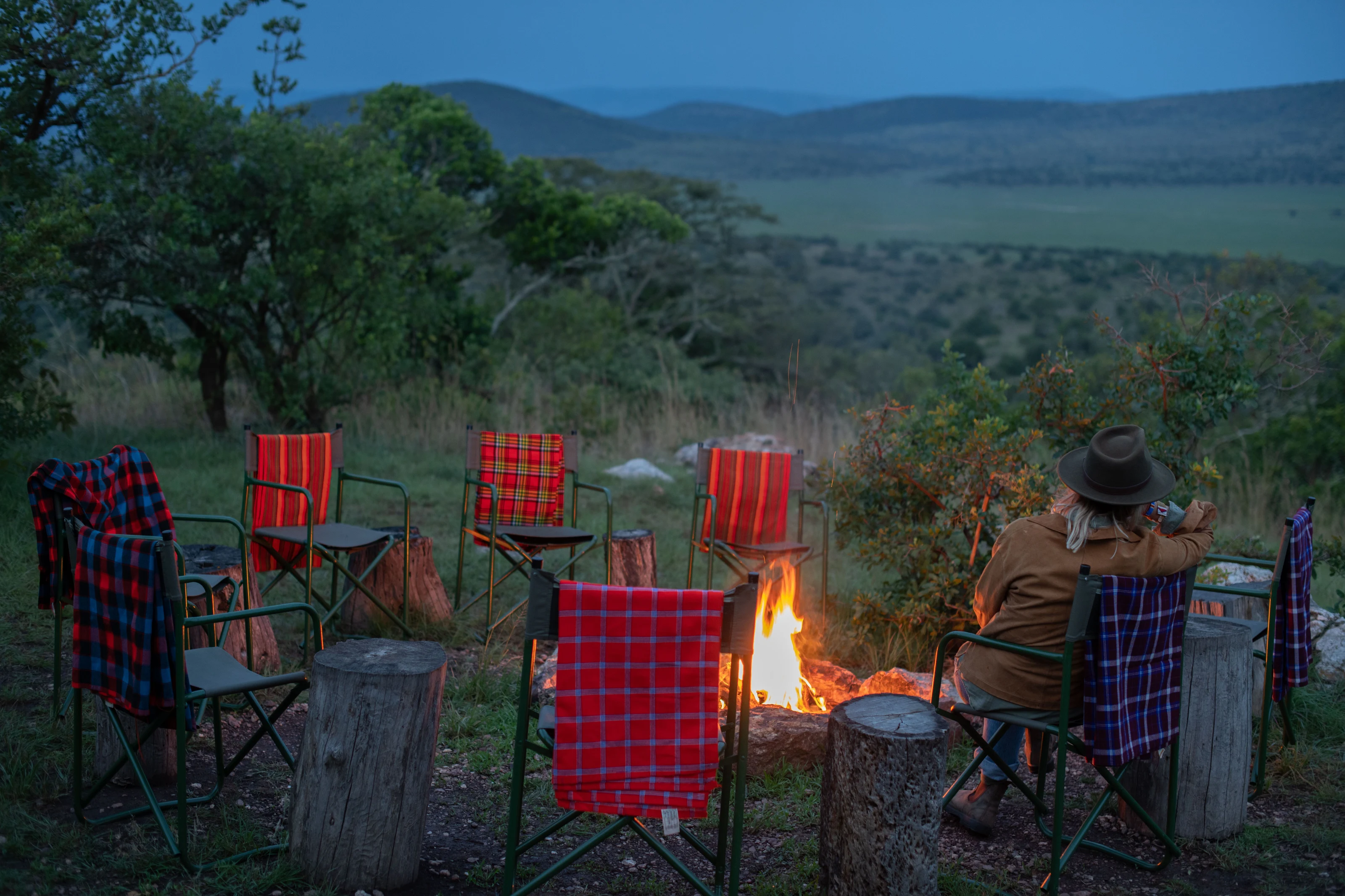 Guests enjoying evening campfire at Karenge Bush Camp with red camping chairs overlooking Akagera National Park landscape at dusk