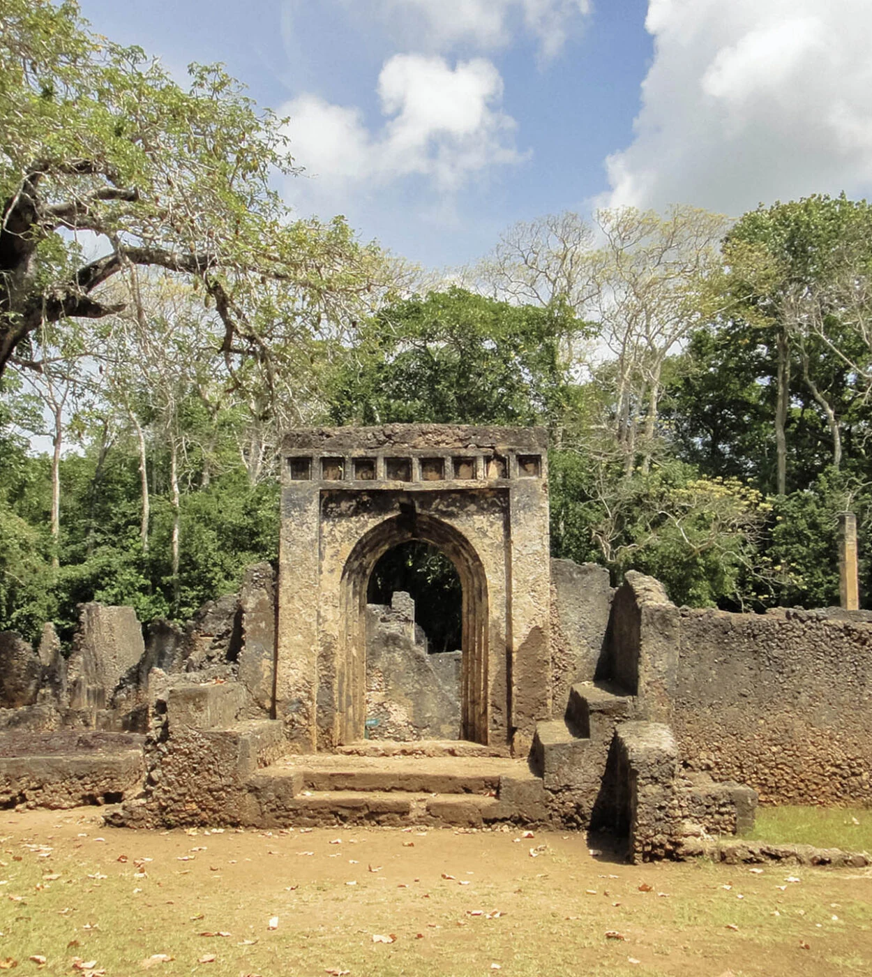 Weathered coral stone arched gateway ruin among trees, portrait