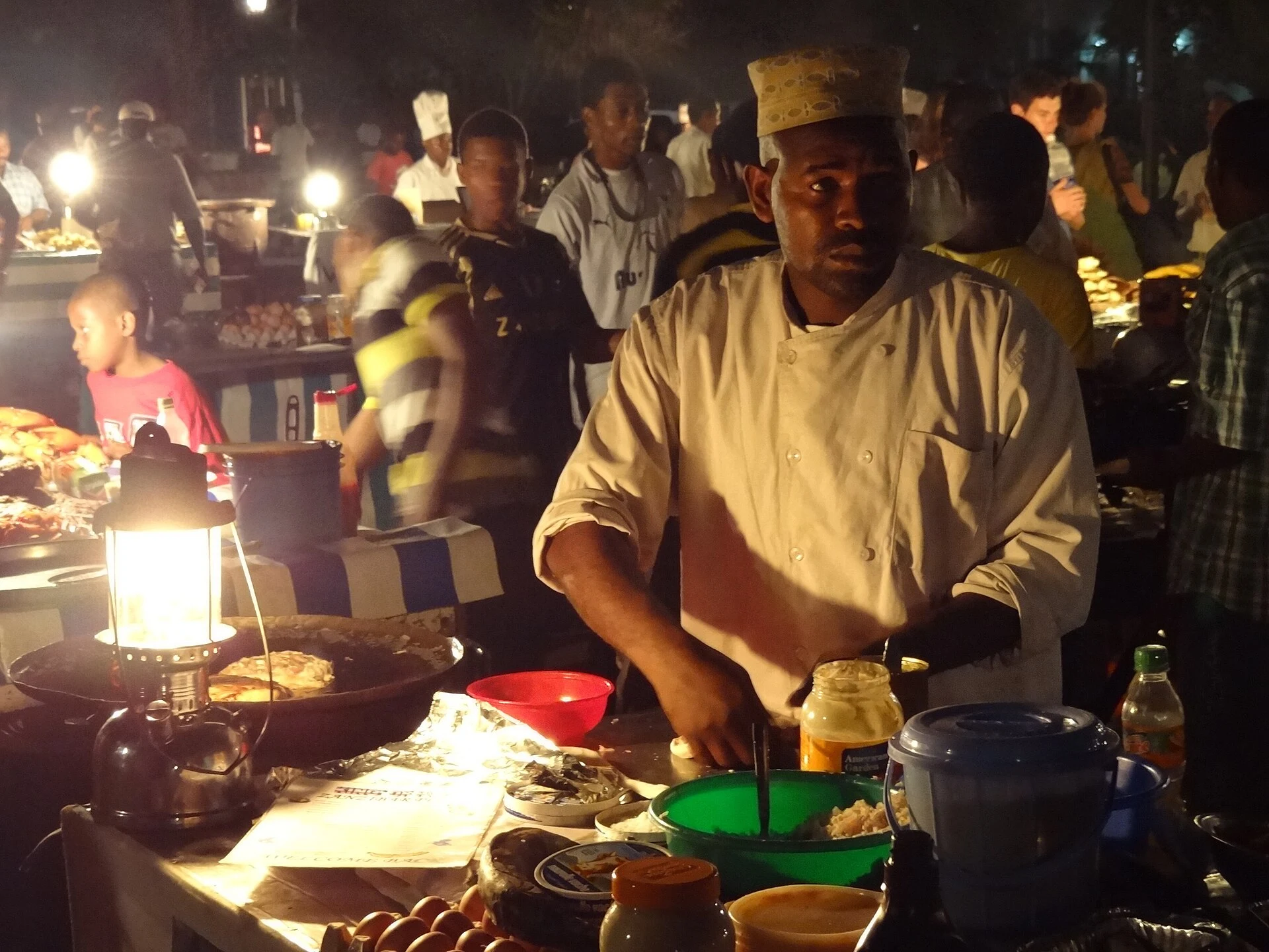 A food vendor cooking by lamplight at the Forodhani Gardens night market