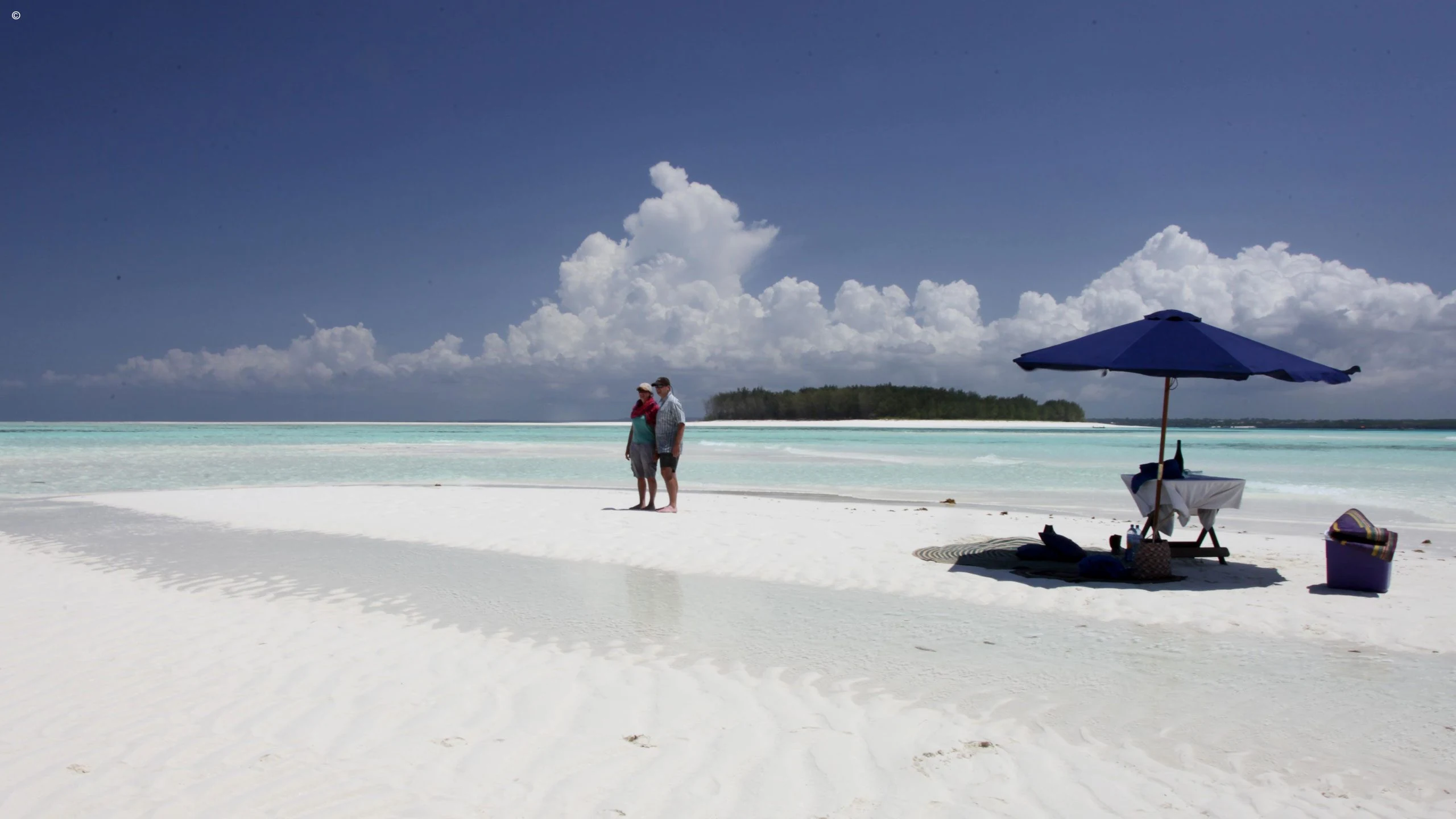 Couple and umbrella on a white sandbank with clouds and clear water