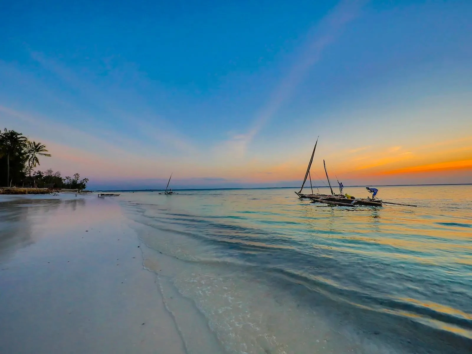 Small sailing boats along a wet sandy beach at sunset