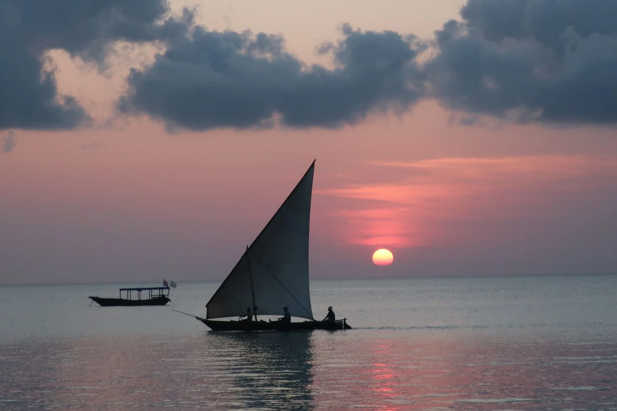 Dhow silhouetted on calm sea at red sunset with a small boat