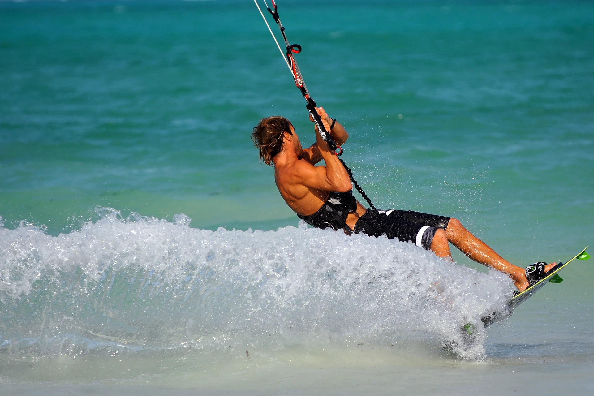A kitesurfer skimming fast through spray across a turquoise lagoon in Zanzibar