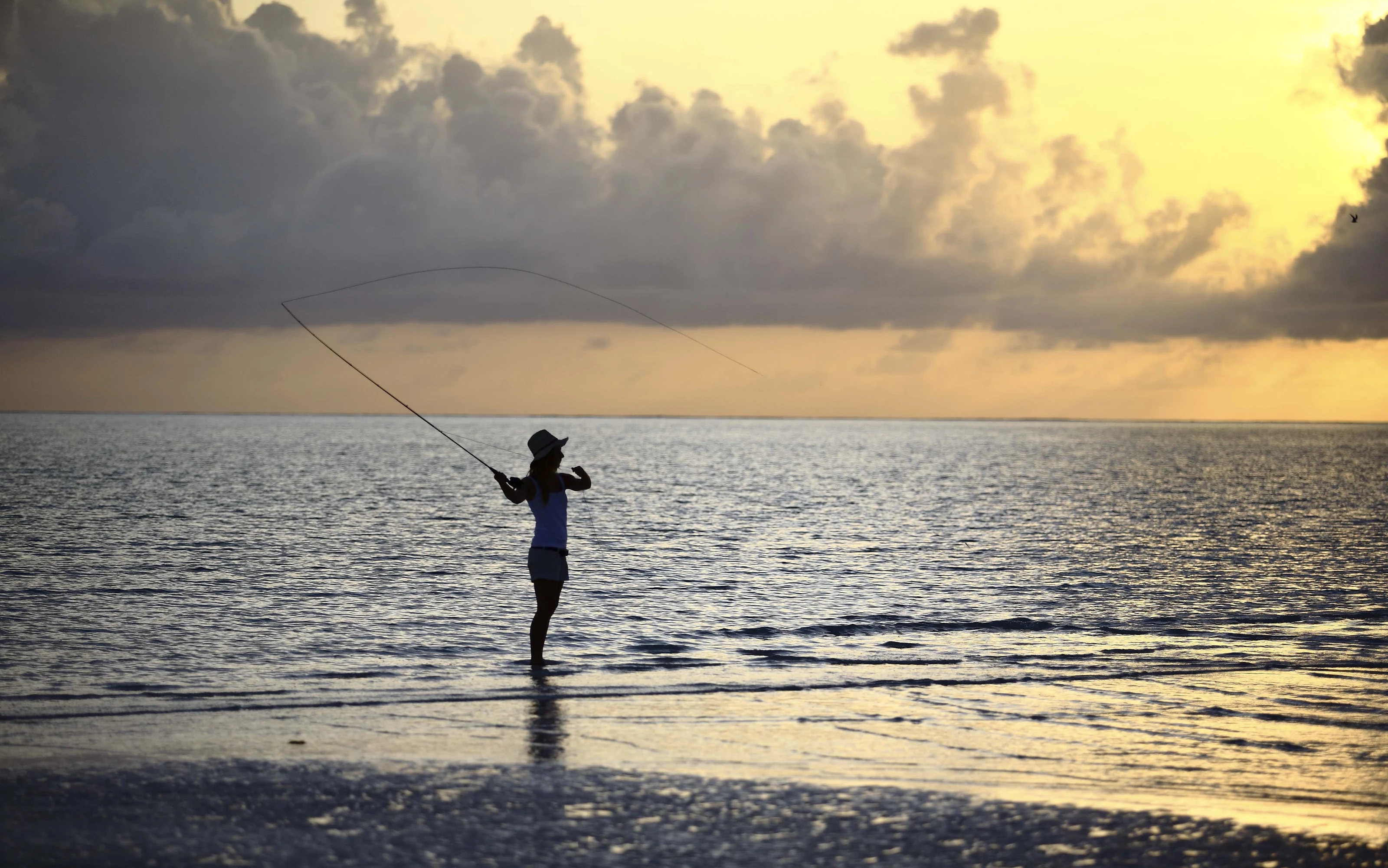 A person fishing from the shallows at dusk off Mnemba Island