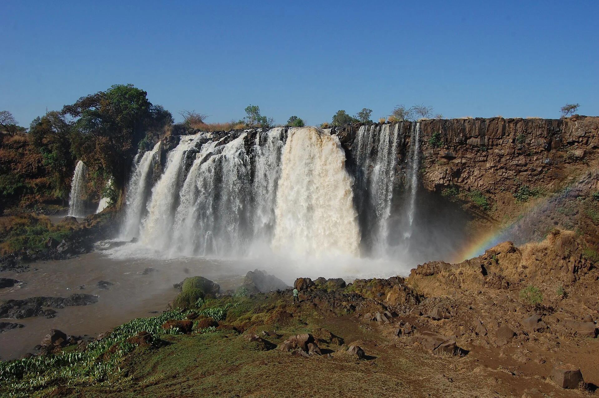The Blue Nile Falls pour over a dark basalt cliff with a rainbow below.