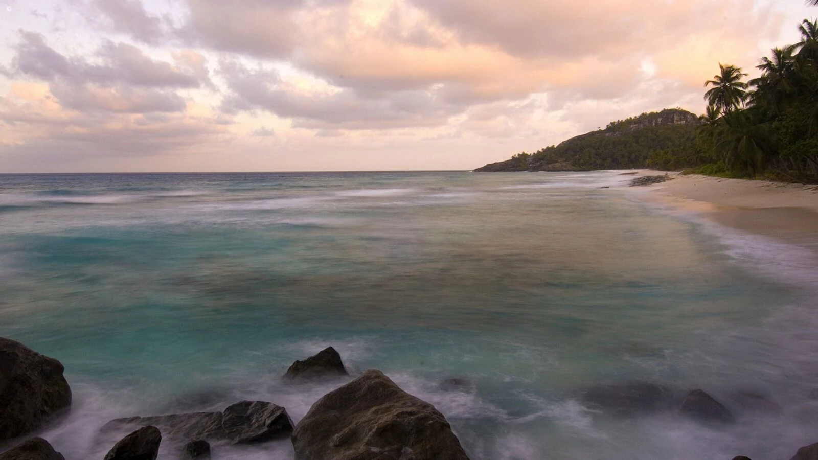 Long exposure shore with dark rocks under pink dusk cloud