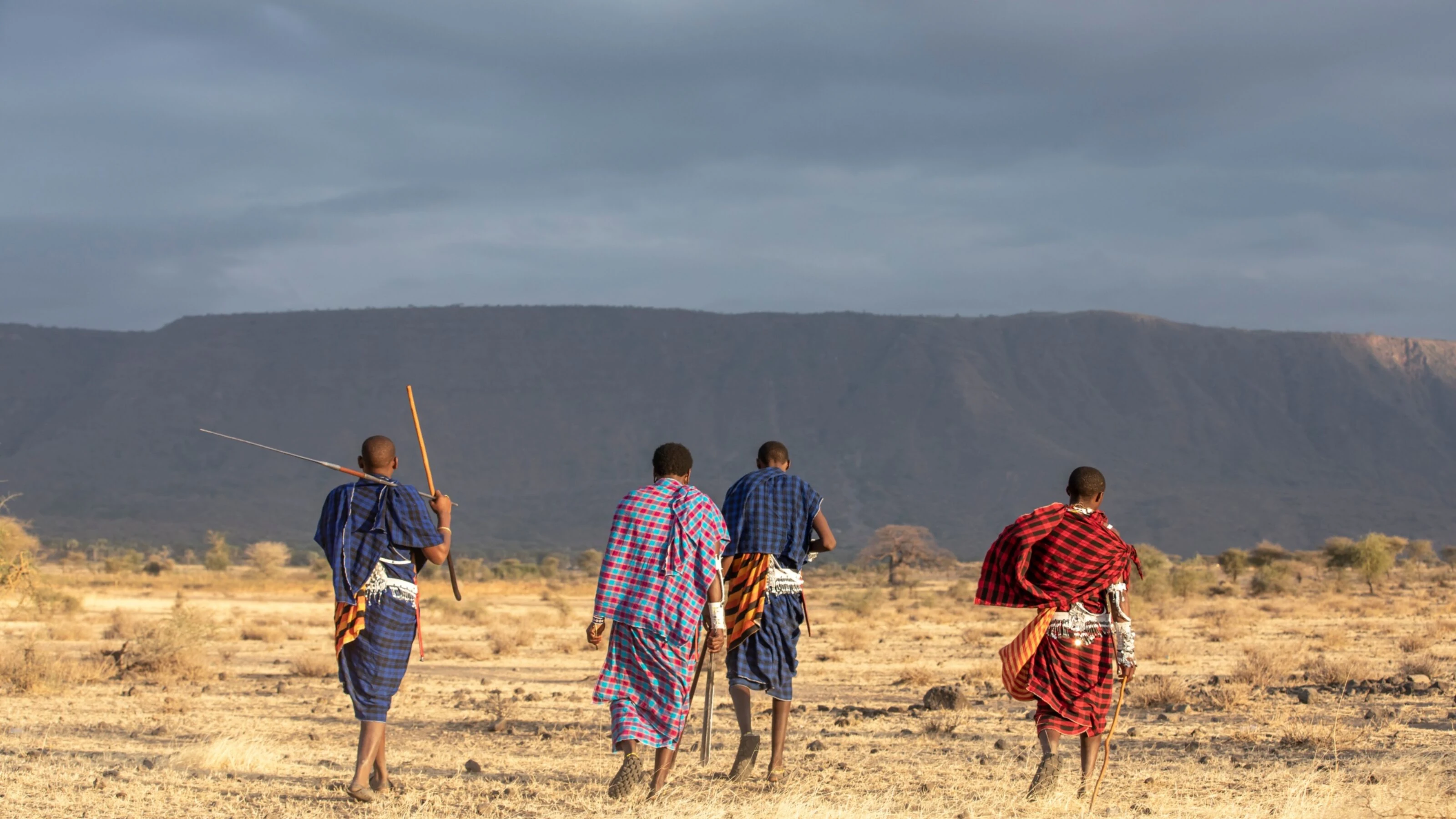 Maasai men walking away across dry plain toward a flat escarpment