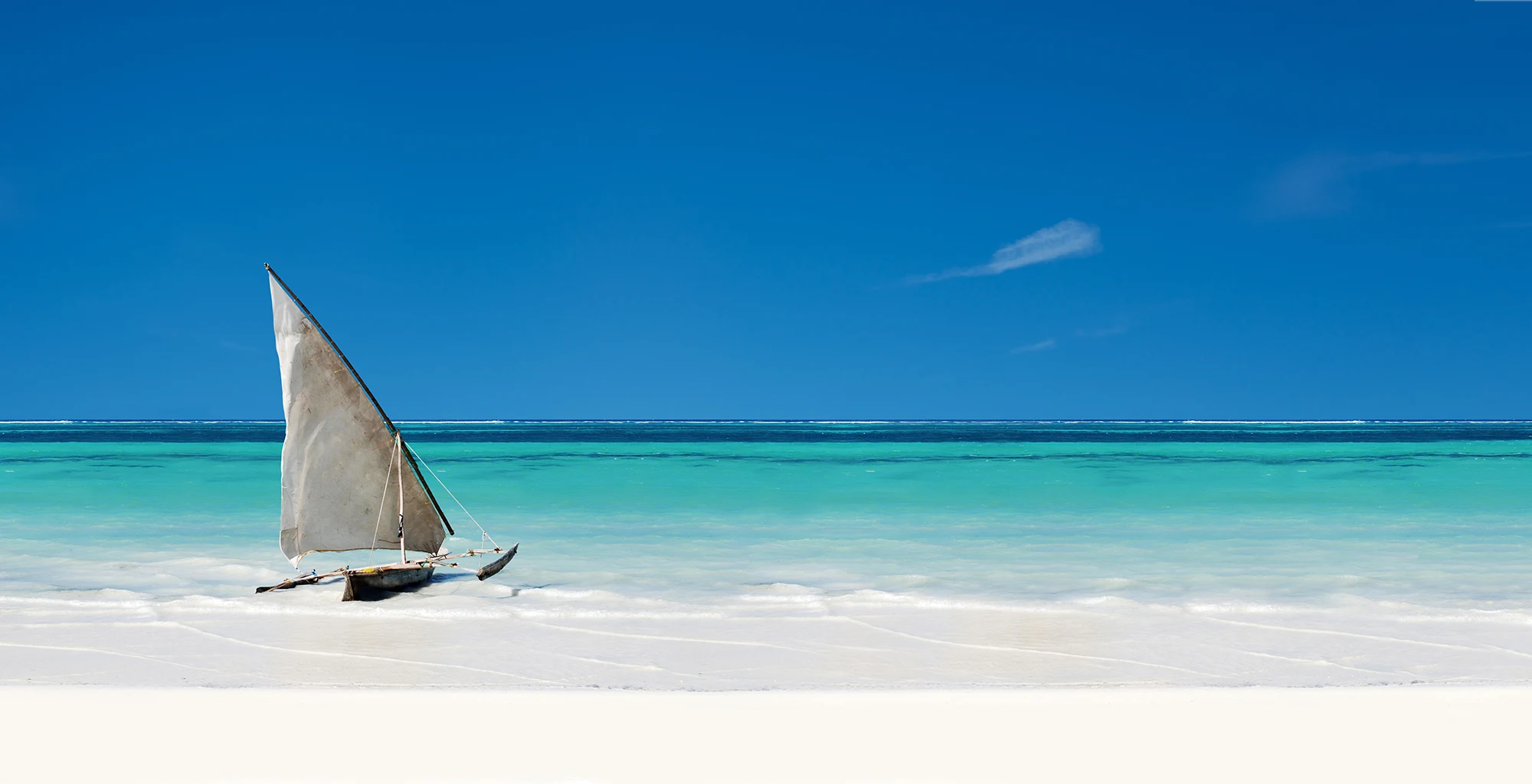 A small sailing dhow pulled up on a white beach beside turquoise water