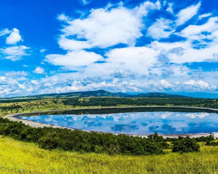 A round crater lake mirroring clouds, ringed by green ridges in Queen Elizabeth National Park