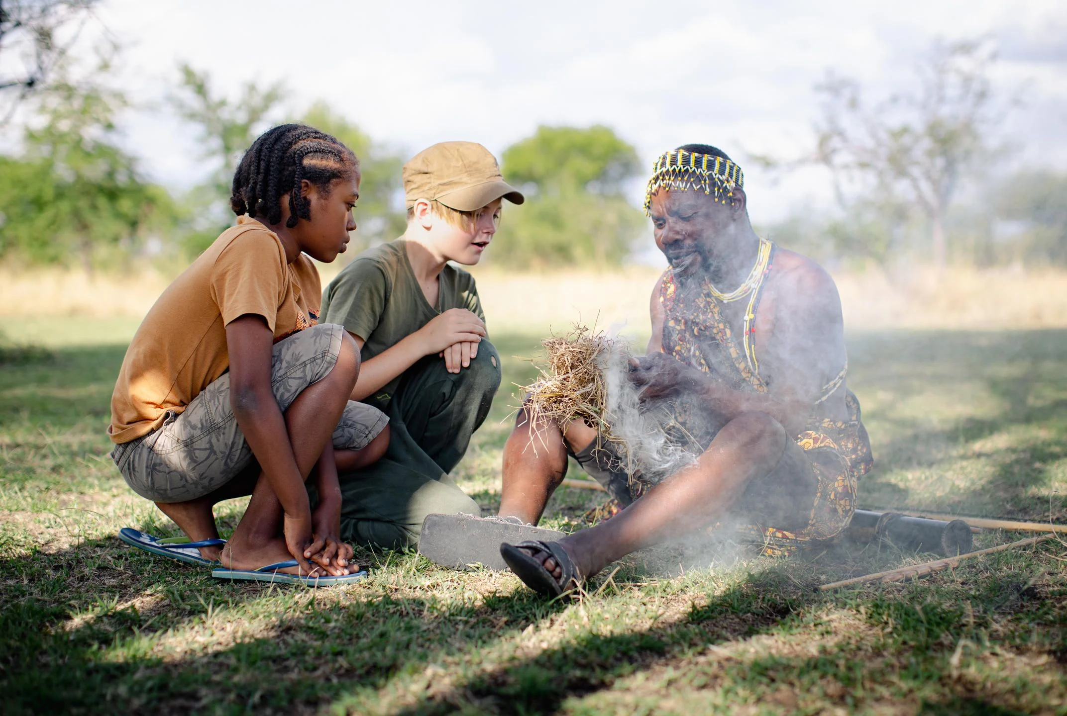 A local guide showing two children how to make fire with sticks