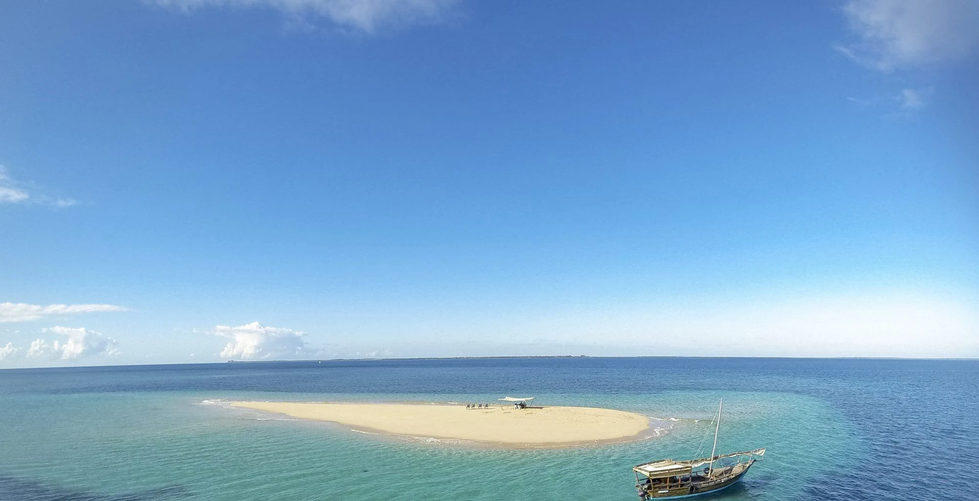 A dhow anchored beside a small white sandbank, seen from the air