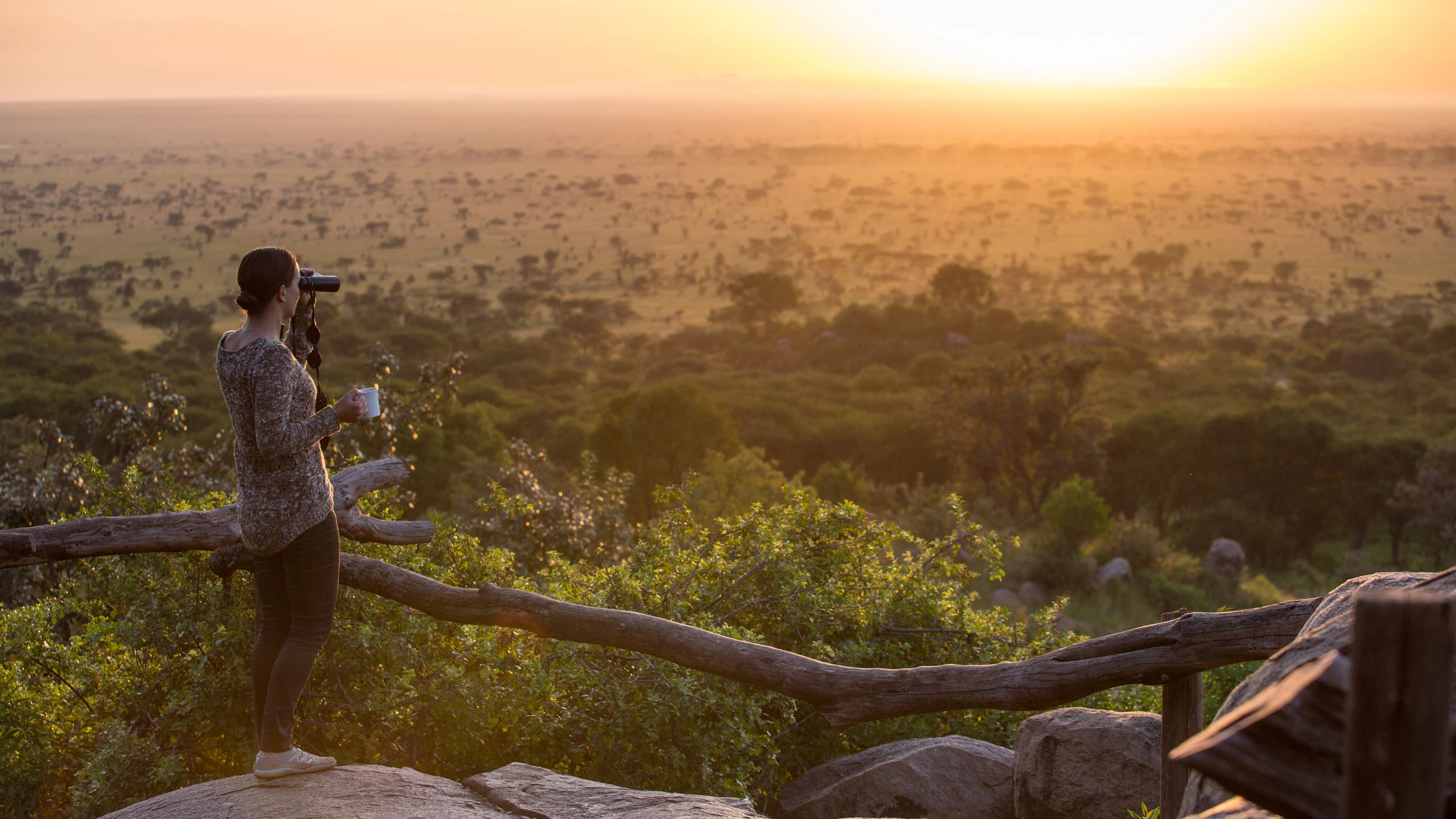 A guest on a rocky outcrop scanning the Serengeti at sunrise