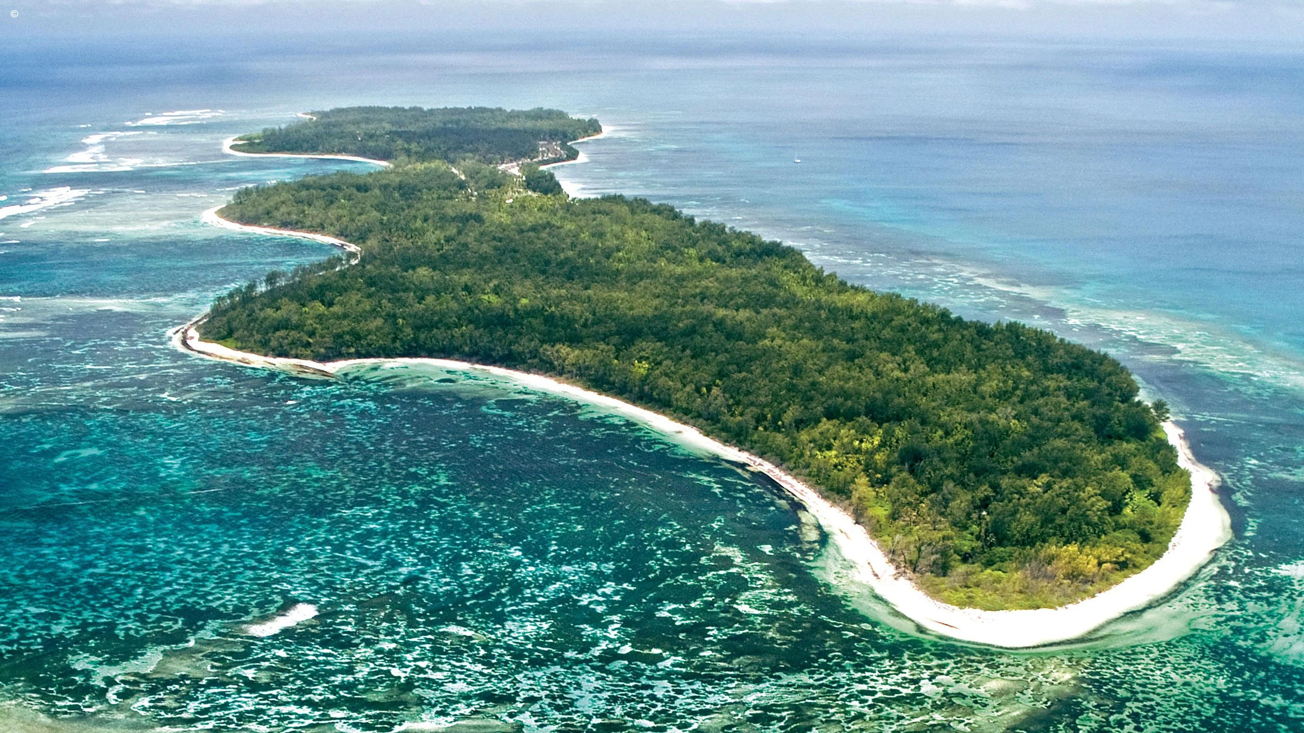 Aerial of a crescent shaped island with reef and white beach