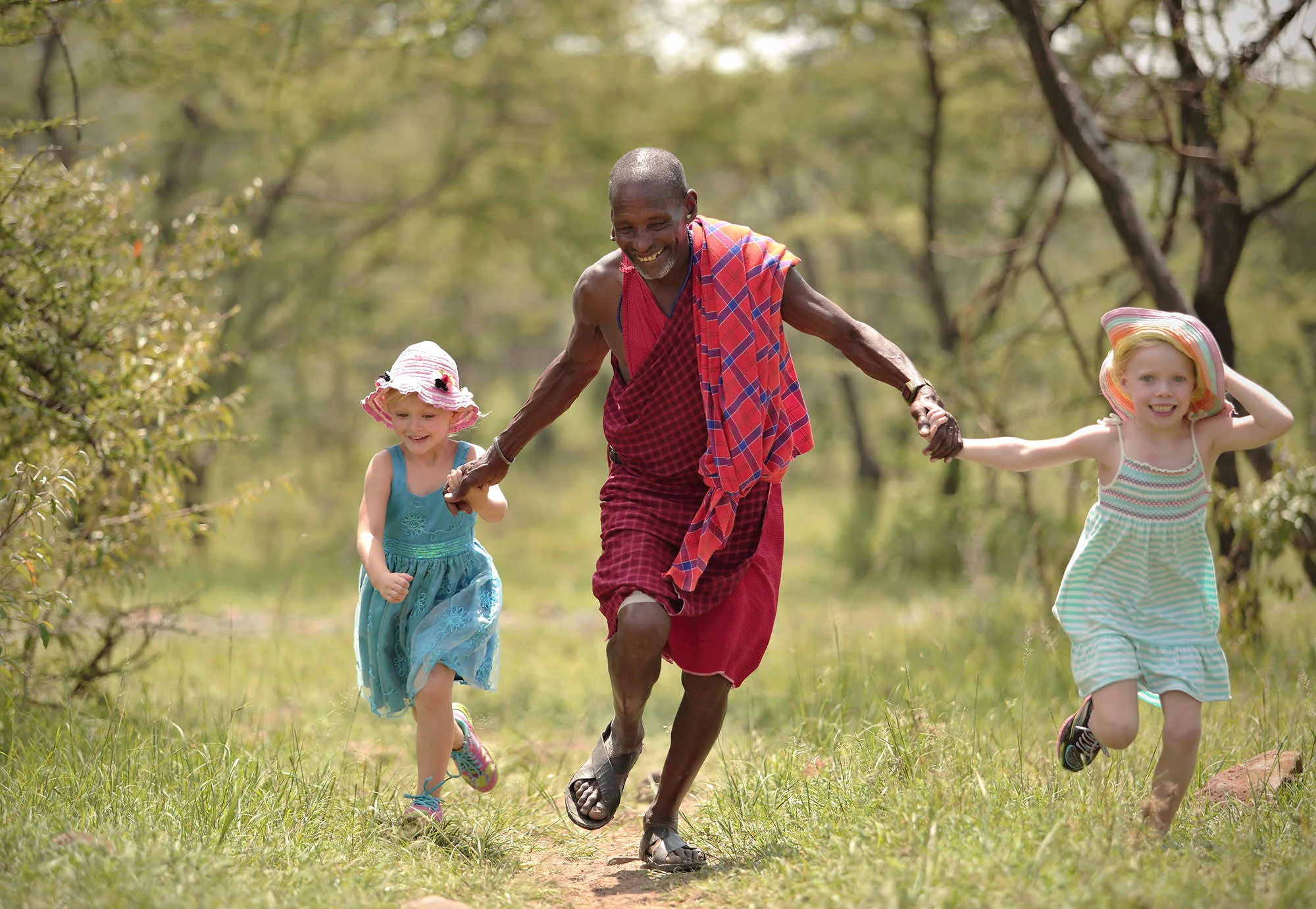 A Maasai host runs hand in hand with two visiting children across open ground