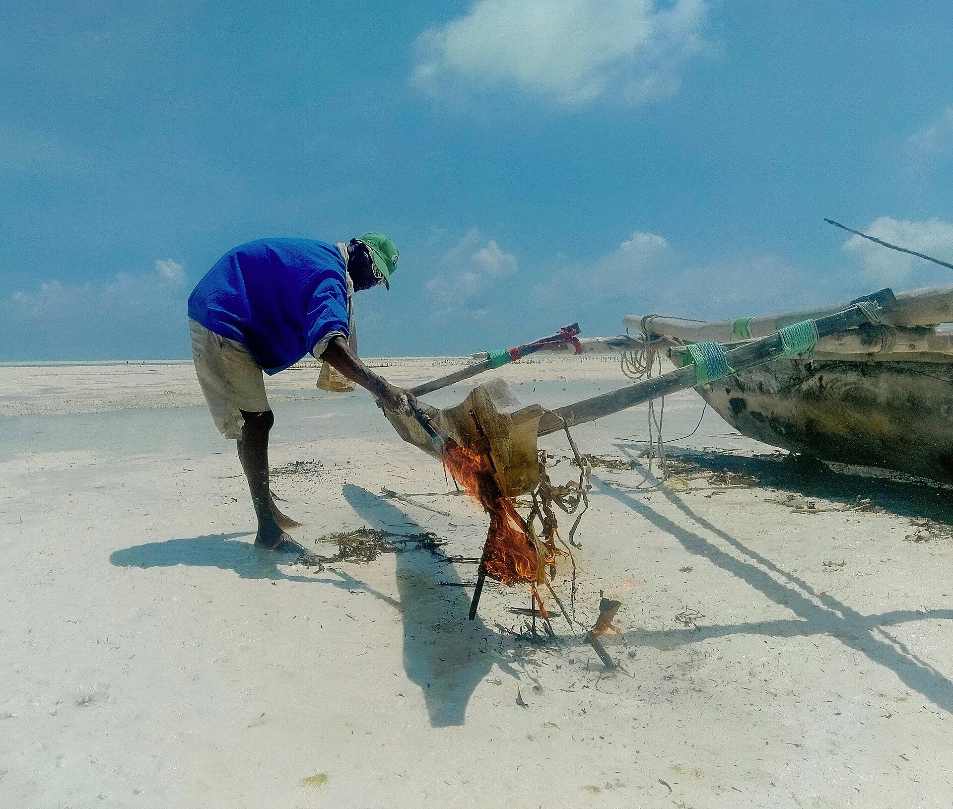 A fisherman working on his wooden outrigger boat on the sand