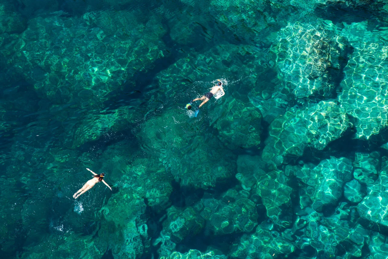 Two snorkellers floating above a shallow coral reef, seen from above