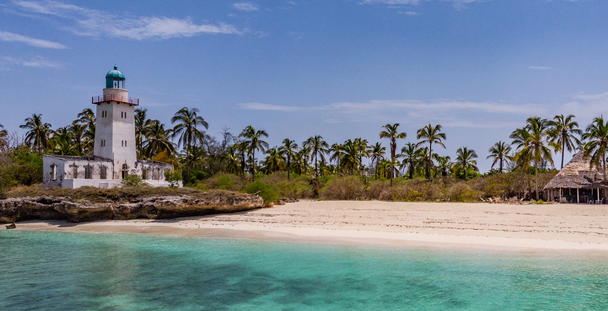 A white lighthouse above palms and a turquoise beach