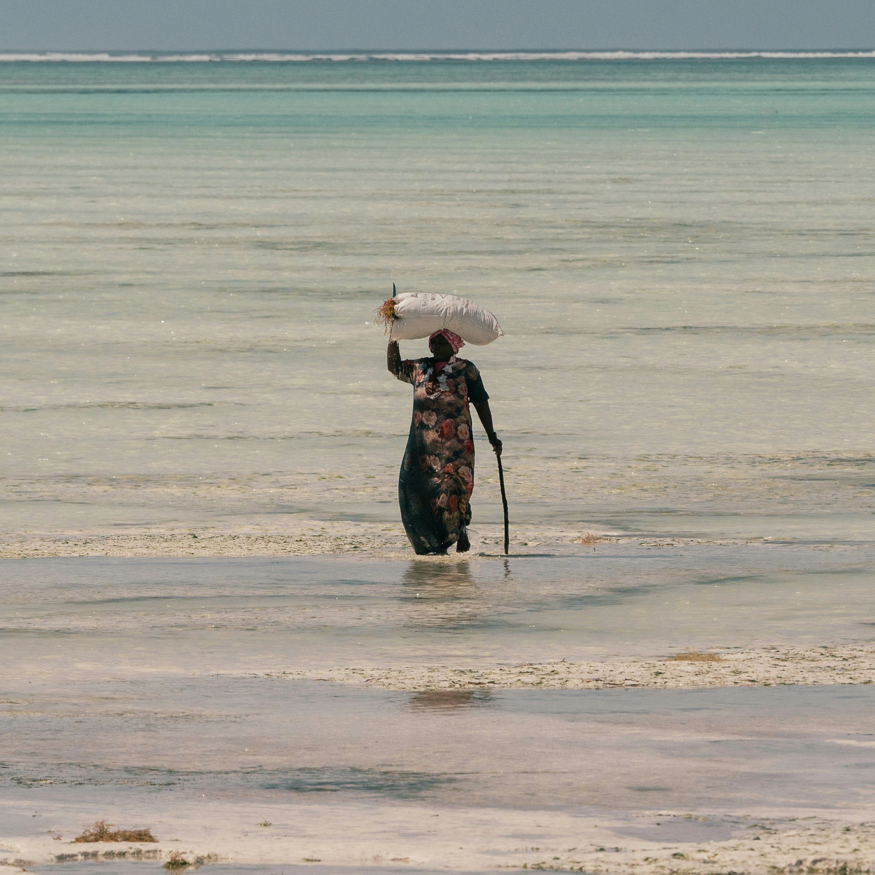 A distant figure wading across a shallow sandy tidal flat
