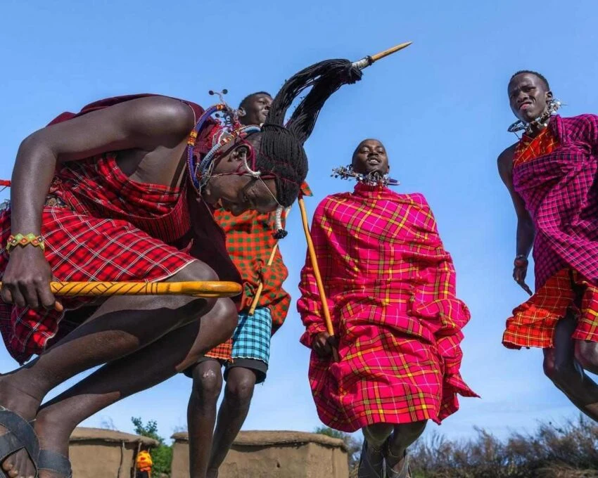 Maasai men in red plaid performing jumping dance under blue sky