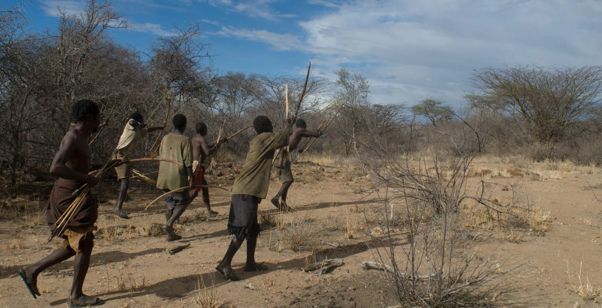 Hadza hunters with bows walking through dry bush near Lake Eyasi